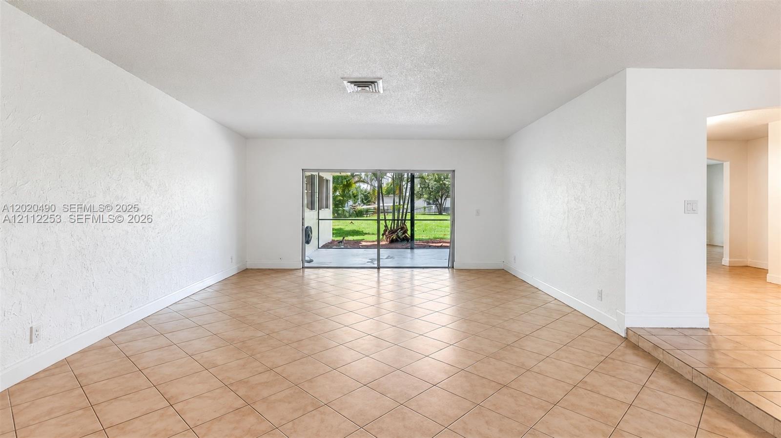 Spacious interior featuring neutral tile flooring, textured wall finishes, and large sliding glass doors opening to a screened outdoor area