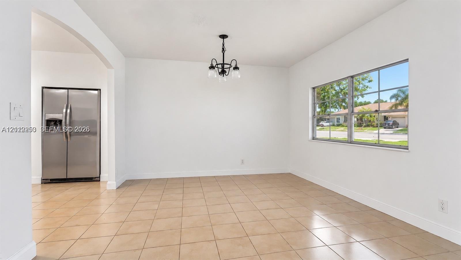 Open interior featuring neutral tile flooring, a multi-pane window, a decorative black metal chandelier, and a stainless steel side-by-side refrigerator