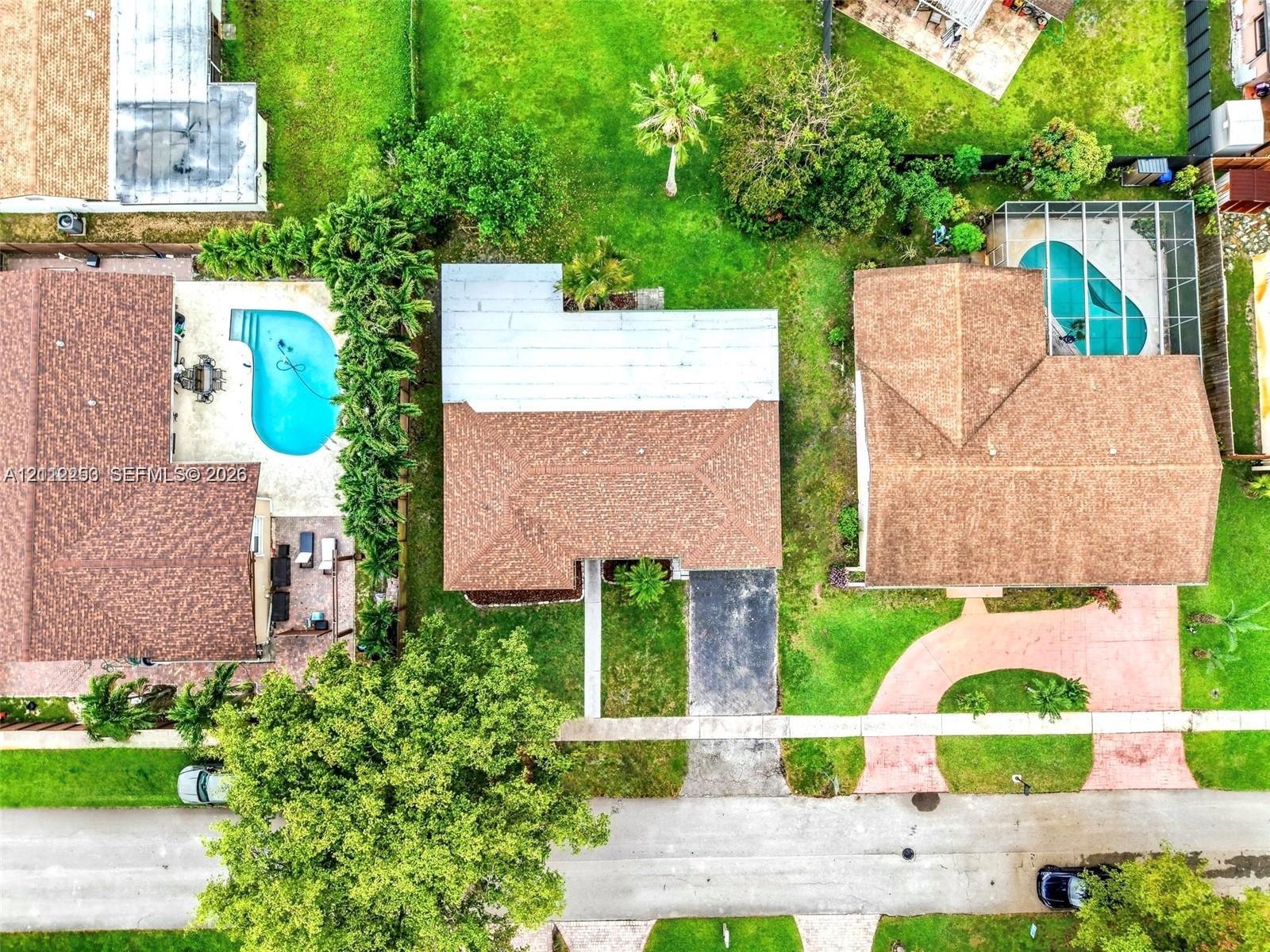 Aerial perspective of a property featuring a shingle roof, paved driveway, and expansive lawn area