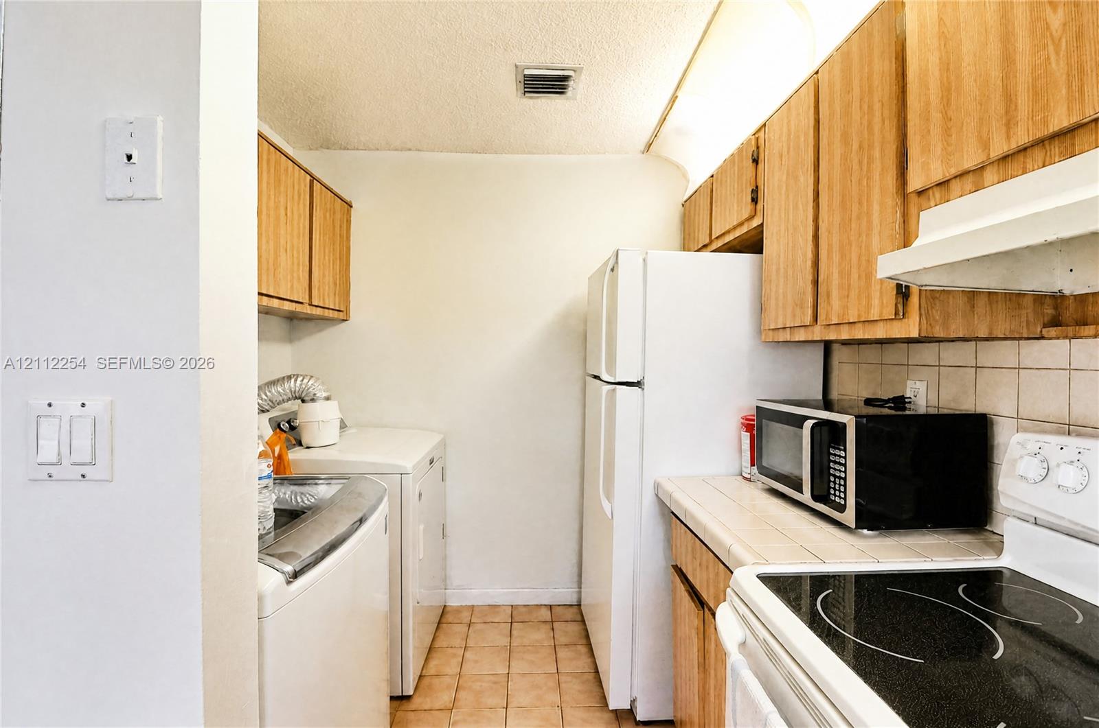 Kitchen featuring wood cabinetry, tile countertops, tile backsplash, and ceramic tile flooring