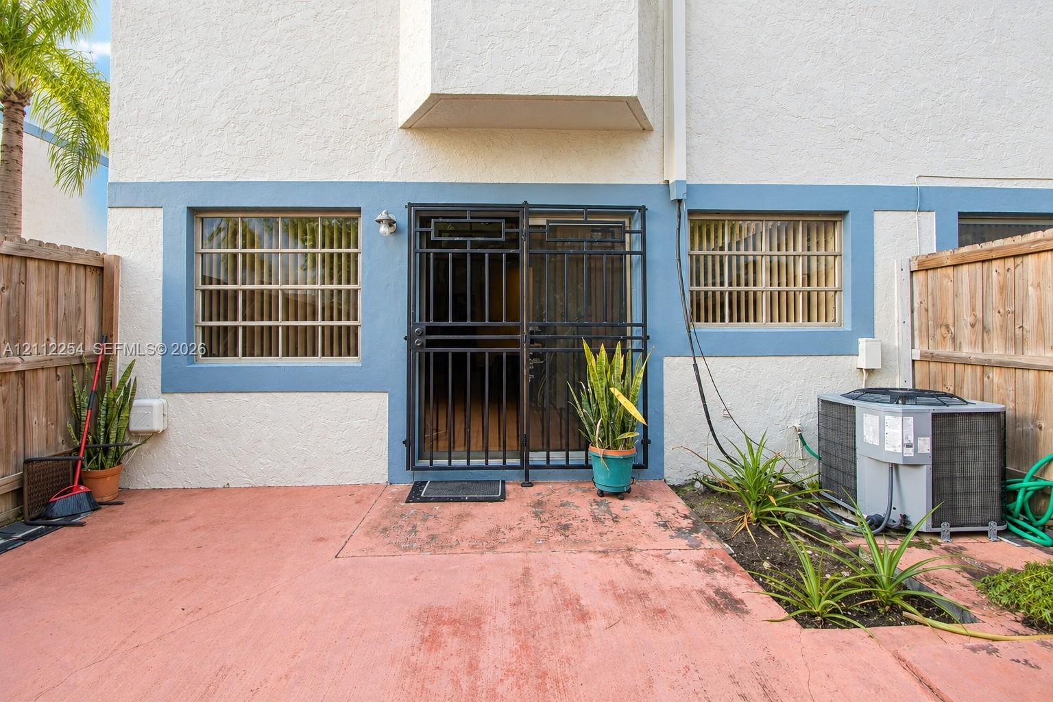 Stucco exterior with accent trim, private rear concrete patio, integrated metal security screen door, and exterior metal window grilles