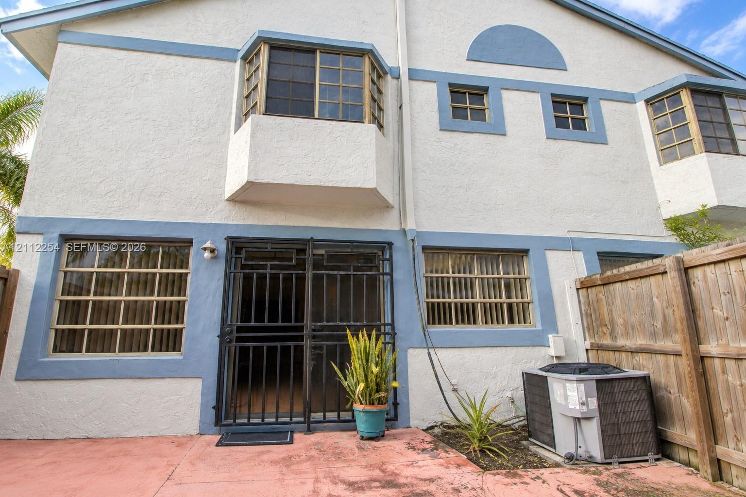 Stucco exterior with multi-level bay windows, grid-patterned glass, integrated security screen door, and exterior heating and cooling unit