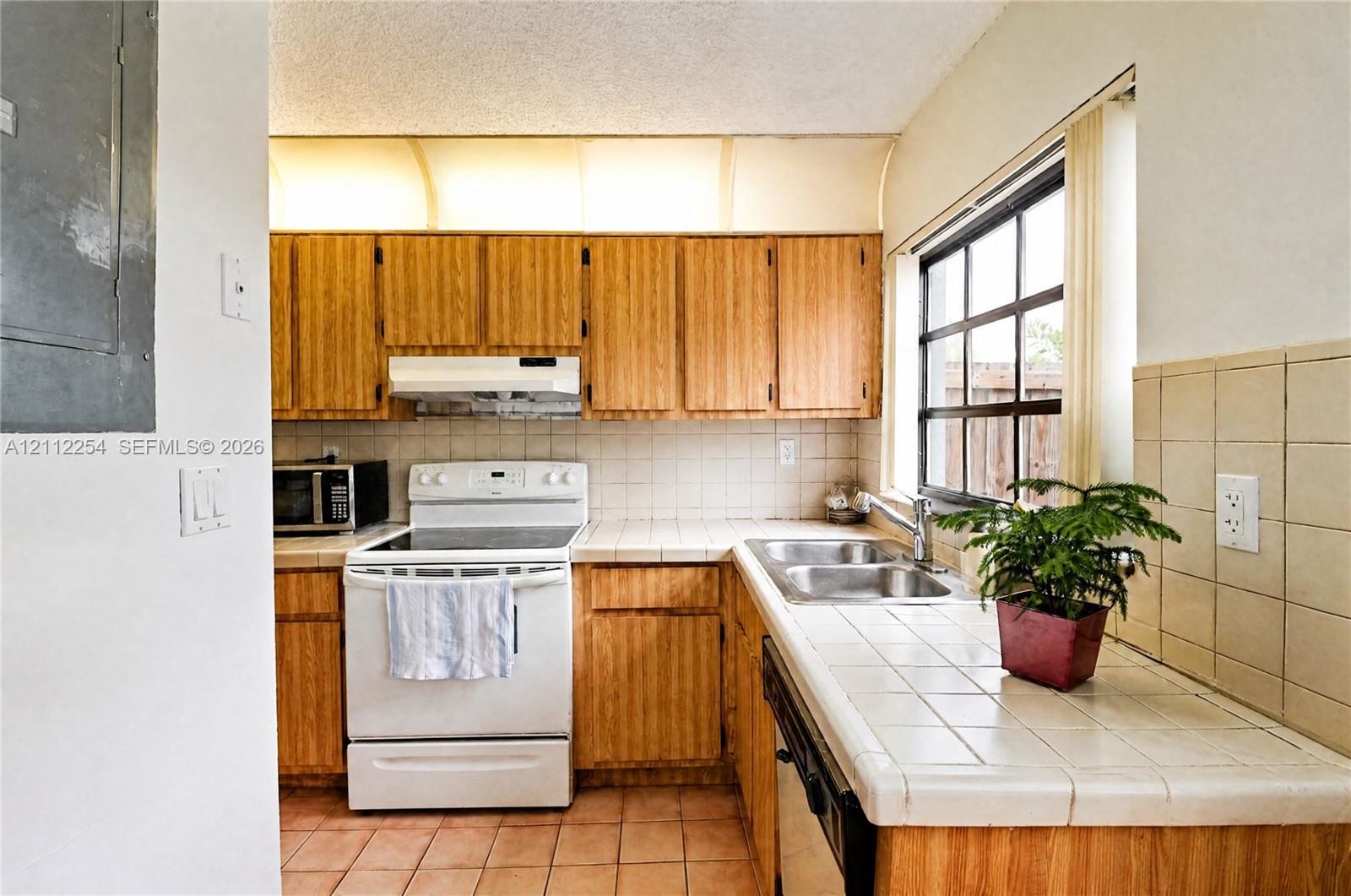 Kitchen featuring wooden cabinetry, white appliance suite, tiled countertops, and a grid-style window