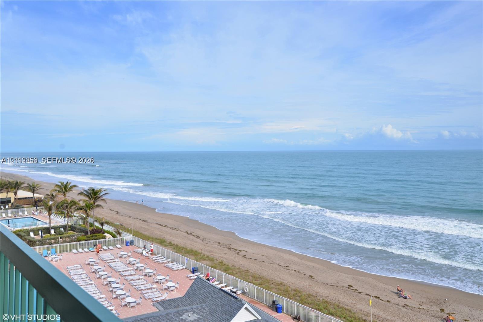 Direct oceanfront perspective featuring a paved sun deck, swimming pool, perimeter fencing, and sand beach access