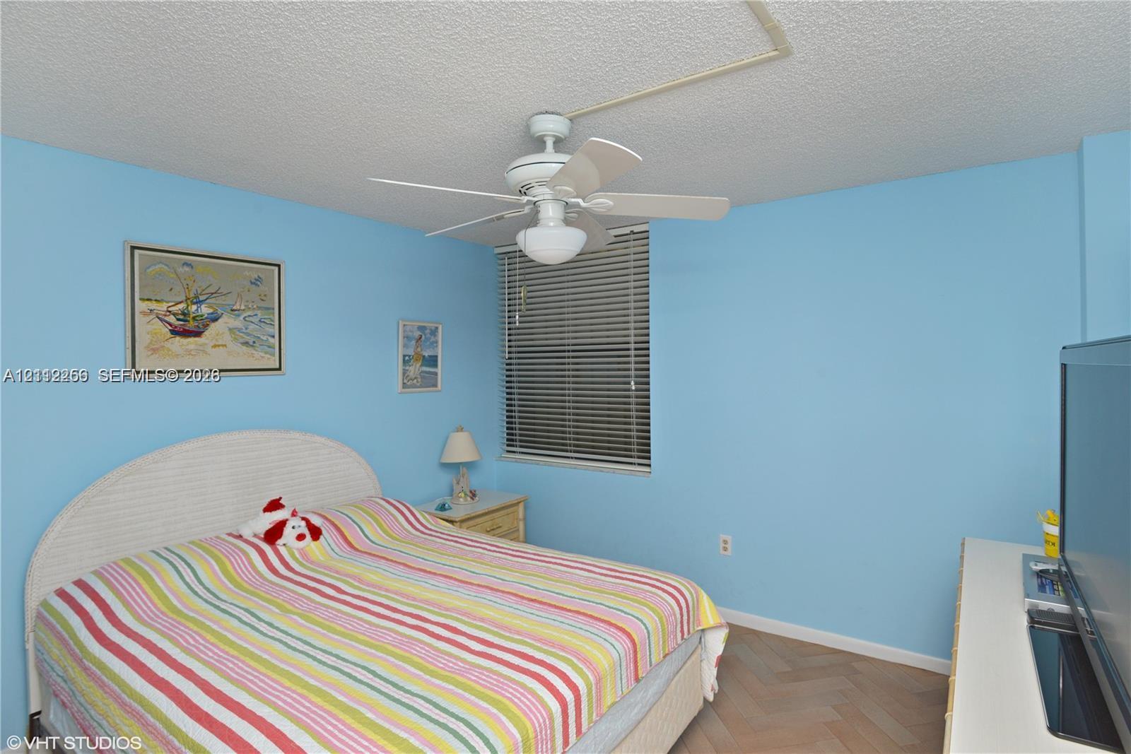 Room featuring wood-finish herringbone flooring, a ceiling fan with integrated lighting, and horizontal window blinds