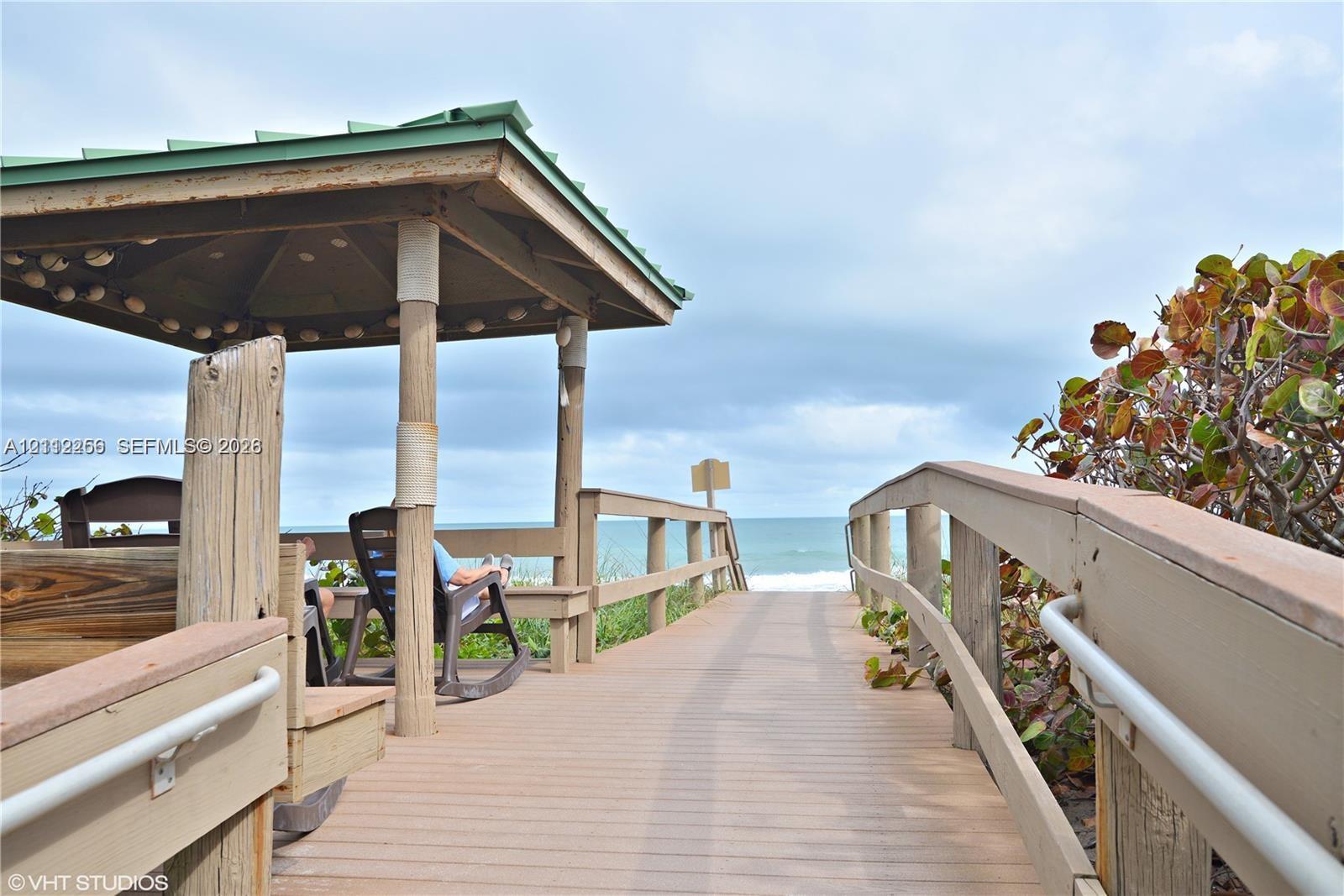 Covered wooden gazebo featuring structural posts, a wooden boardwalk, and perimeter railings