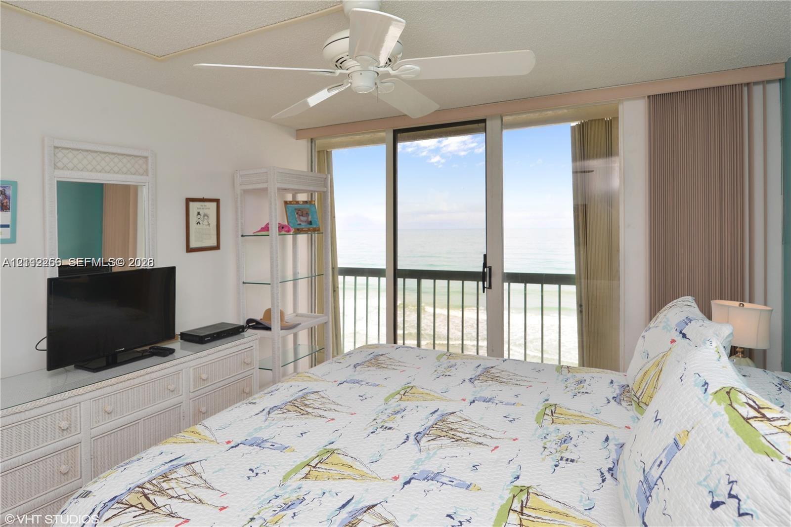 Sliding glass doors opening to a balcony with metal railings and ocean water backdrop, ceiling fan, and wall-mounted mirror