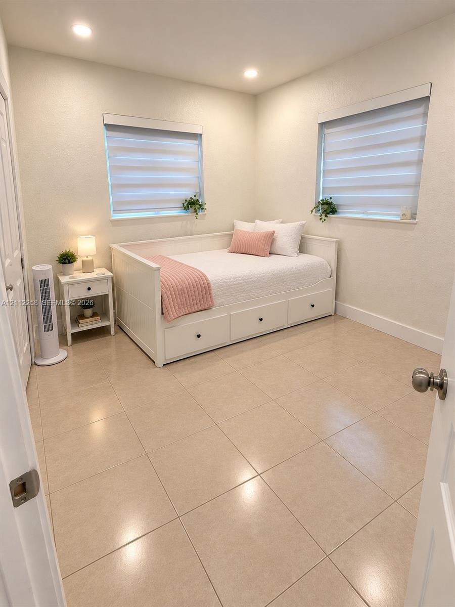 Neutral-toned tile flooring, recessed ceiling lighting, and dual windows with installed roller shades