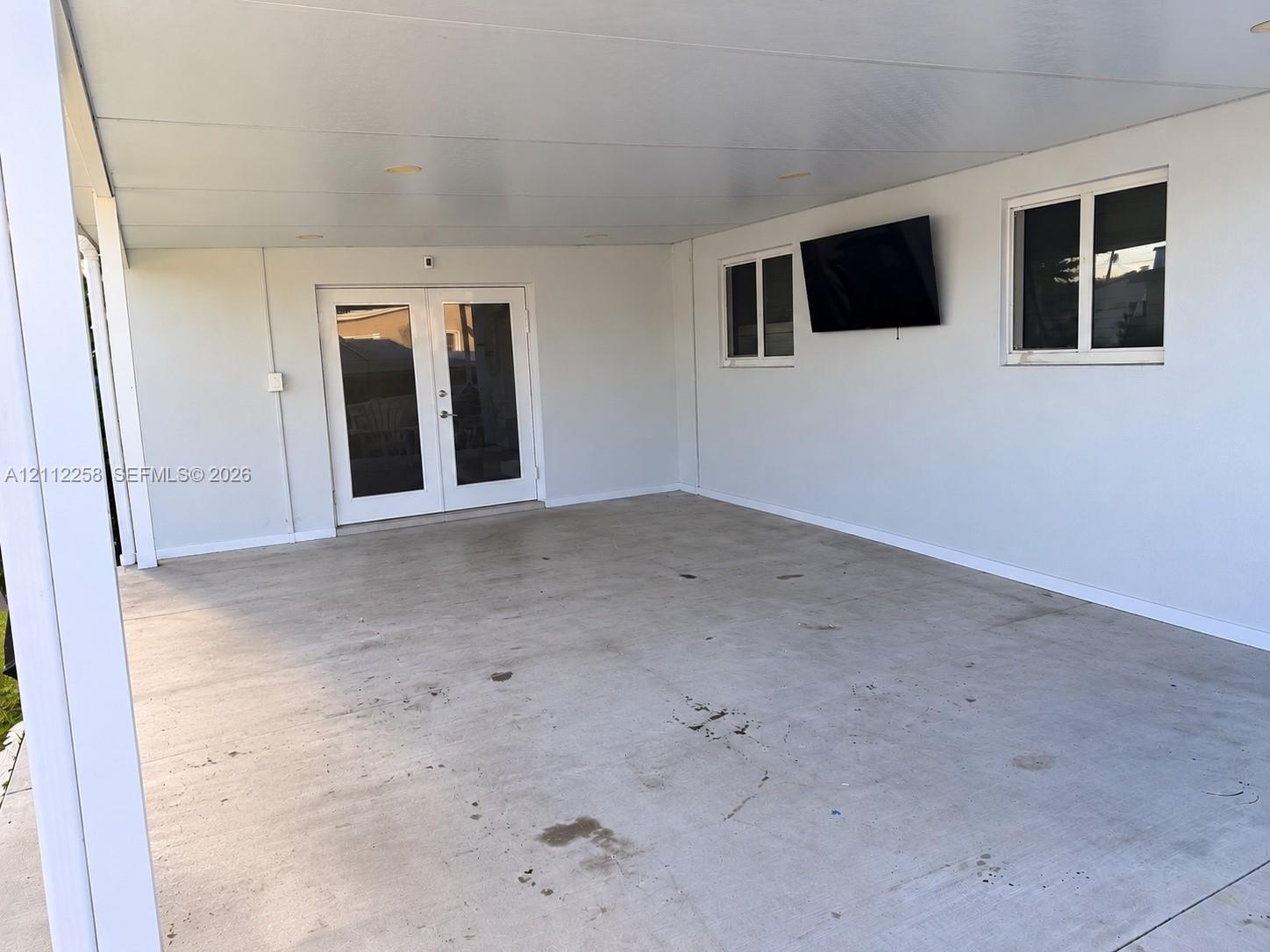 Covered patio featuring a concrete floor, recessed ceiling lighting, wall-mounted television, and glass-paneled double doors Covered patio featuring a concrete floor, recessed ceiling lighting, wall-mounted television, and glass-paneled double doors