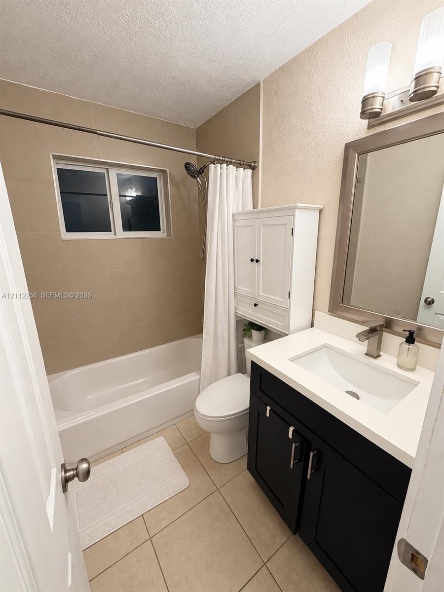 Bathroom featuring a dark-finish vanity with a white countertop and rectangular undermount sink, wall-mounted white cabinetry, tile flooring, and a shower-tub combination with tile surround Bathroom featuring a dark-finish vanity with a white countertop and rectangular undermount sink, wall-mounted white cabinetry, tile flooring, and a shower-tub combination with tile surround