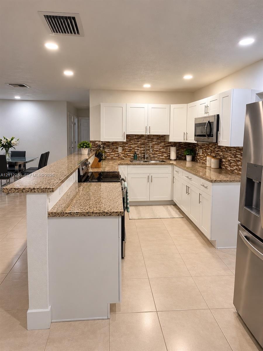 Kitchen featuring white shaker-style cabinetry, stone-finish countertops, tile backsplash, stainless steel appliances, and tile flooring Kitchen featuring white shaker-style cabinetry, stone-finish countertops, tile backsplash, stainless steel appliances, and tile flooring
