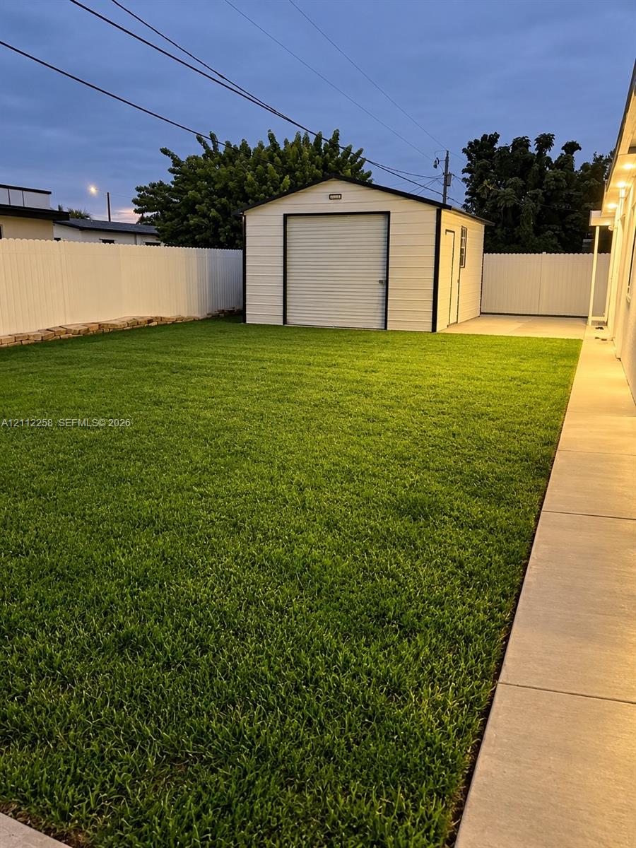 Backyard featuring a manicured lawn, white vinyl fencing, detached metal structure, and a concrete pathway