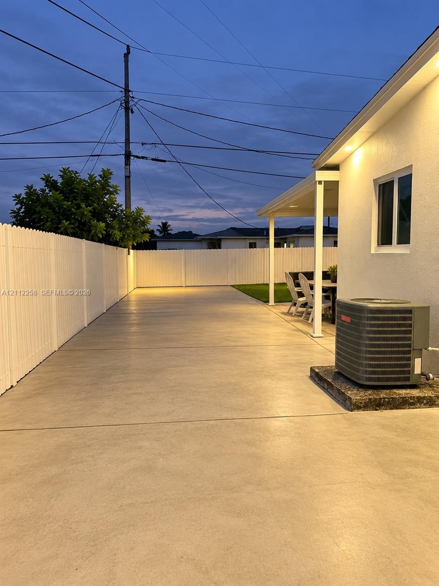 Extensive concrete patio featuring a covered area, enclosed by white vinyl fencing and illuminated by recessed soffit lighting