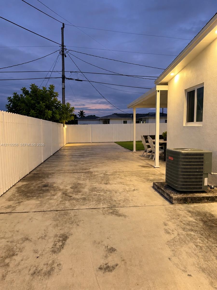 Concrete side patio featuring a covered overhang, enclosed by a white vinyl privacy fence with integrated recessed soffit lighting