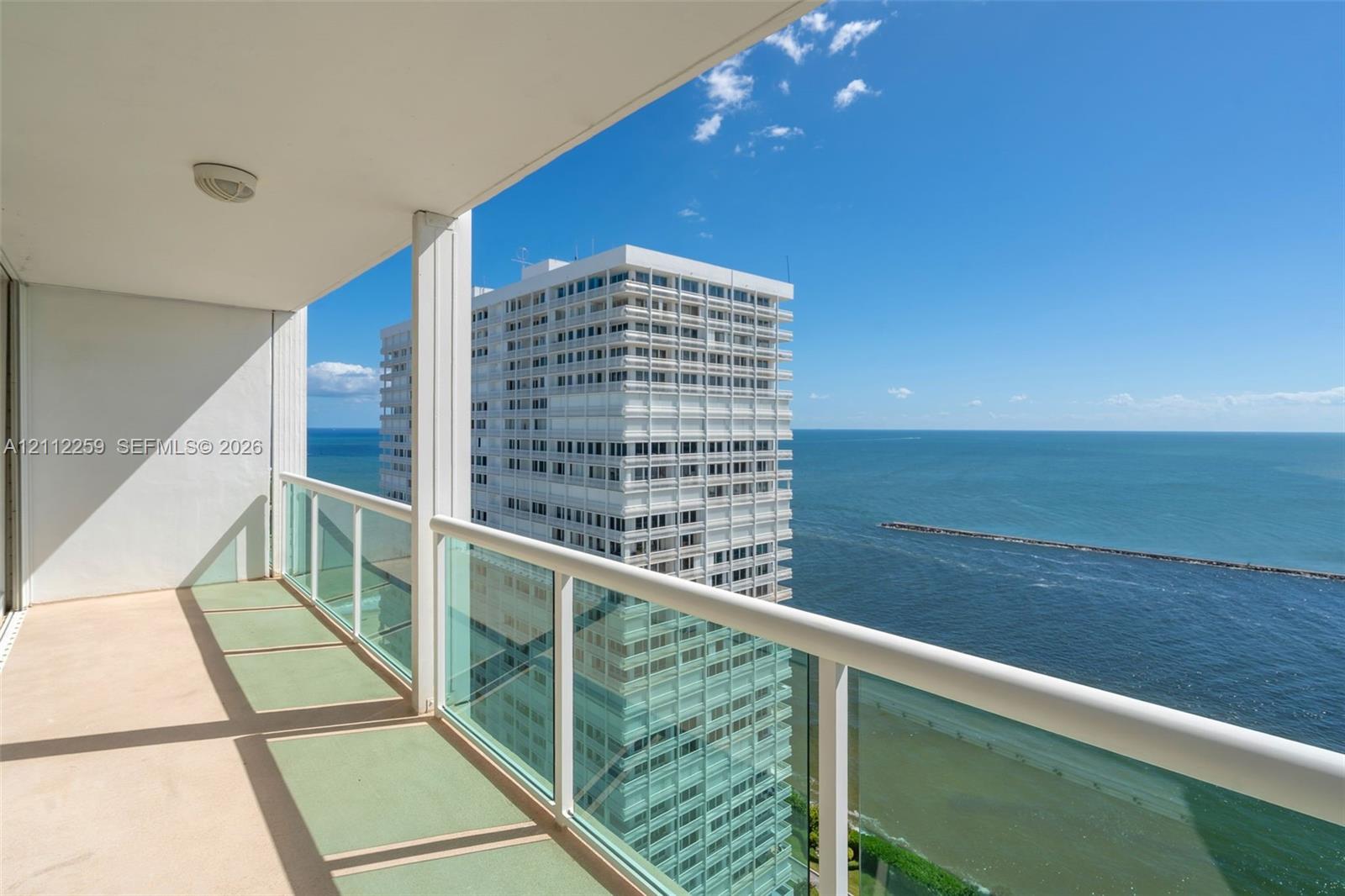 Covered balcony featuring glass pane railings, solid support columns, and water horizon exposure Covered balcony featuring glass pane railings, solid support columns, and water horizon exposure