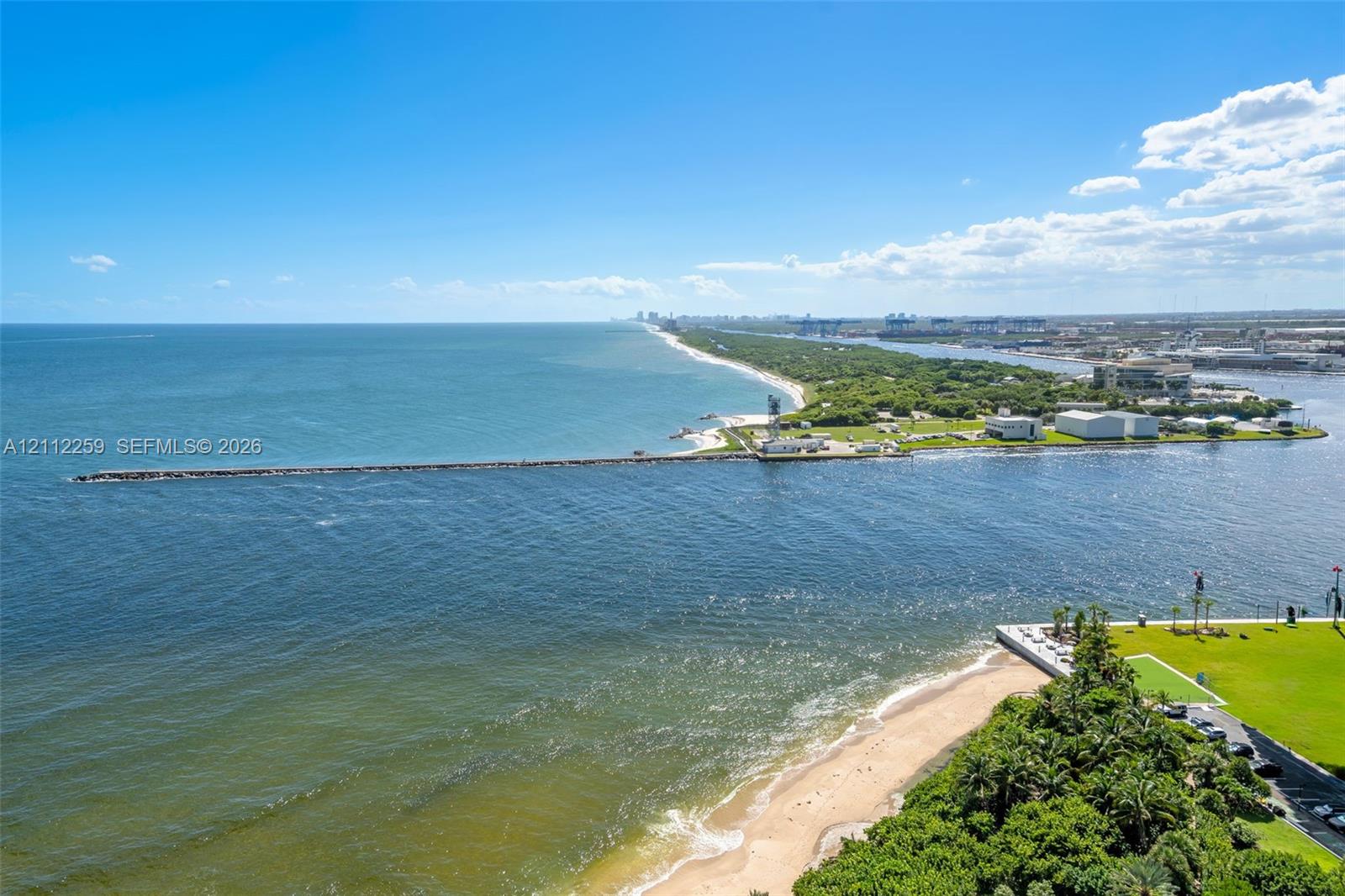 Aerial perspective featuring a direct coastal shoreline, expansive open water, a paved jetty, and manicured green space Aerial perspective featuring a direct coastal shoreline, expansive open water, a paved jetty, and manicured green space