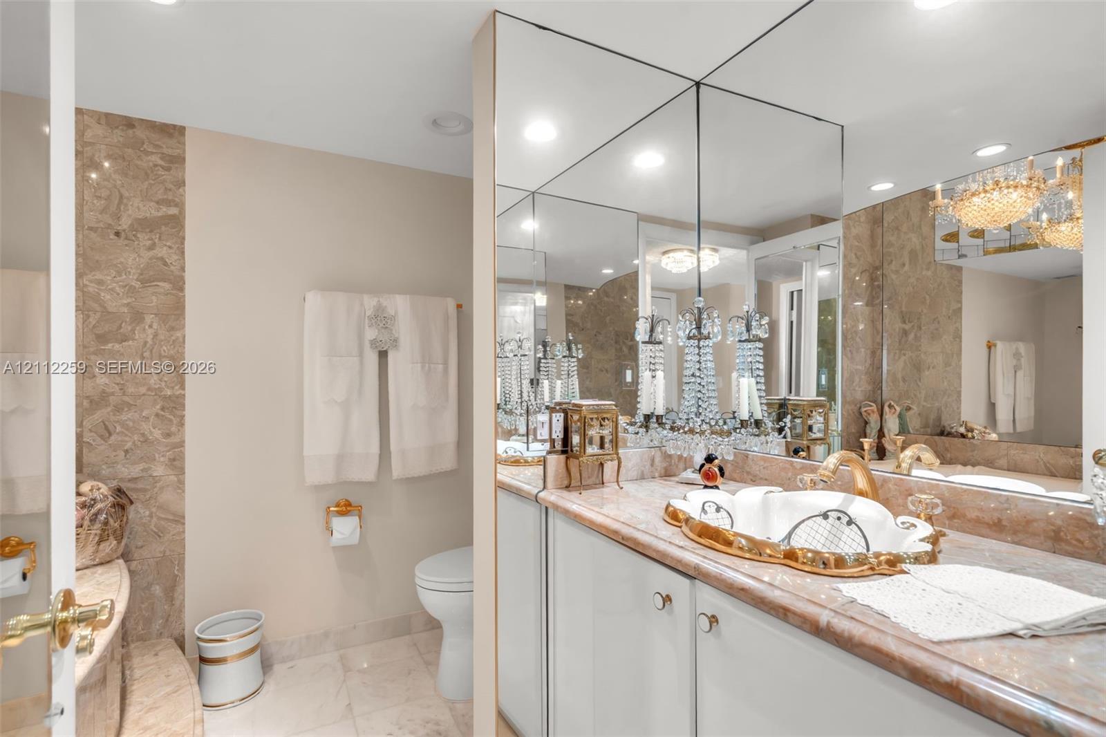 Vanity featuring a custom-shaped basin with gold-tone trim, integrated stone countertop, floor-to-ceiling mirror, and wall-mounted crystal chandelier-style lighting