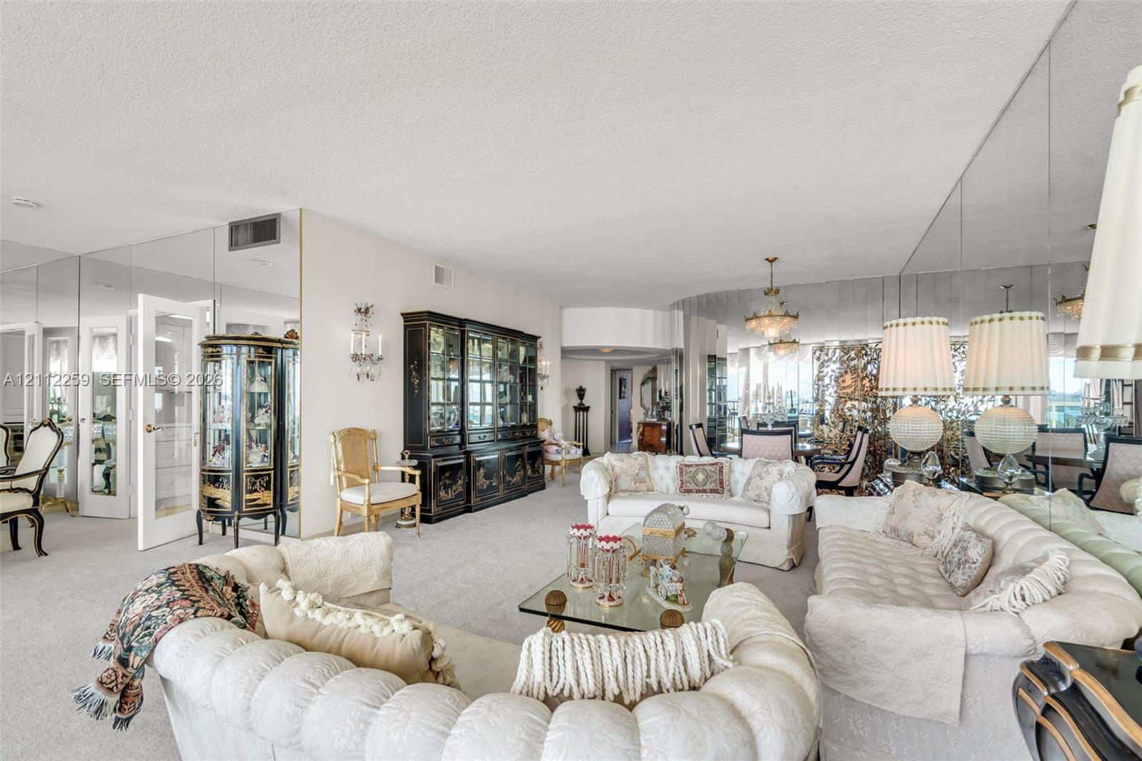 Expansive living space featuring wall-to-wall mirrored surfaces, a built-in floor-to-ceiling cabinet, dual multi-tiered chandeliers, and neutral wall-to-wall carpeting