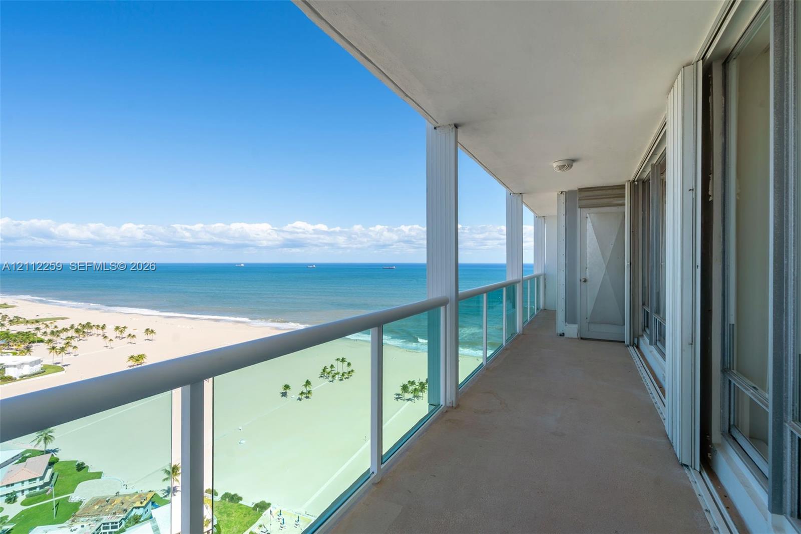 Covered balcony featuring glass-panel railings, solid surface flooring, and oceanfront exposure Covered balcony featuring glass-panel railings, solid surface flooring, and oceanfront exposure