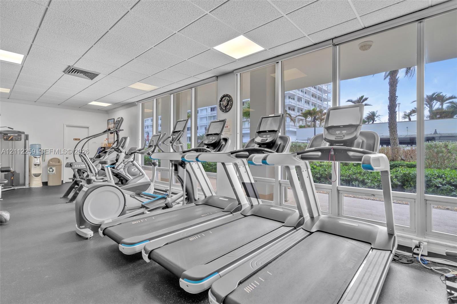 Fitness center featuring rubber flooring, drop ceiling with recessed lighting, and a wall of floor-to-ceiling windows