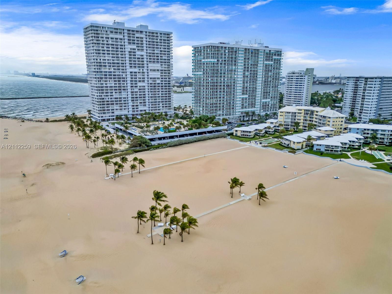 Direct oceanfront location featuring a sprawling sandy beach, clusters of mature palm trees, and elevated multi-story residential towers Direct oceanfront location featuring a sprawling sandy beach, clusters of mature palm trees, and elevated multi-story residential towers