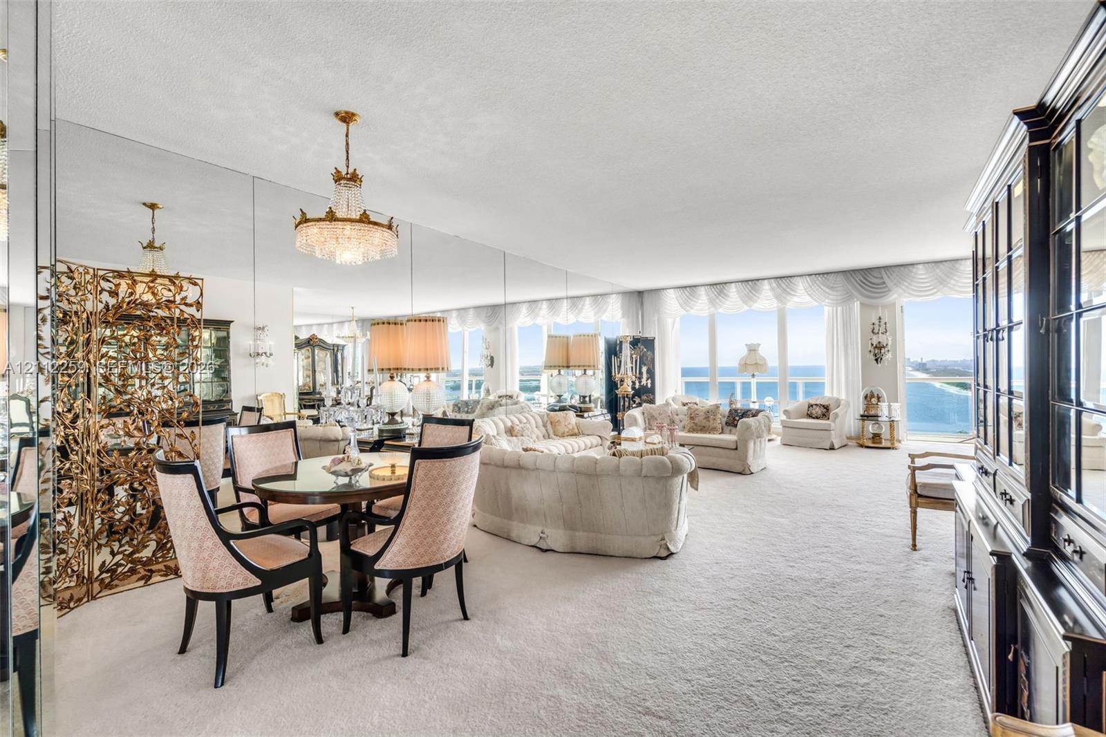 Living area featuring wall-to-wall mirrors, floor-to-ceiling windows with coastal water outlooks, and a crystal chandelier