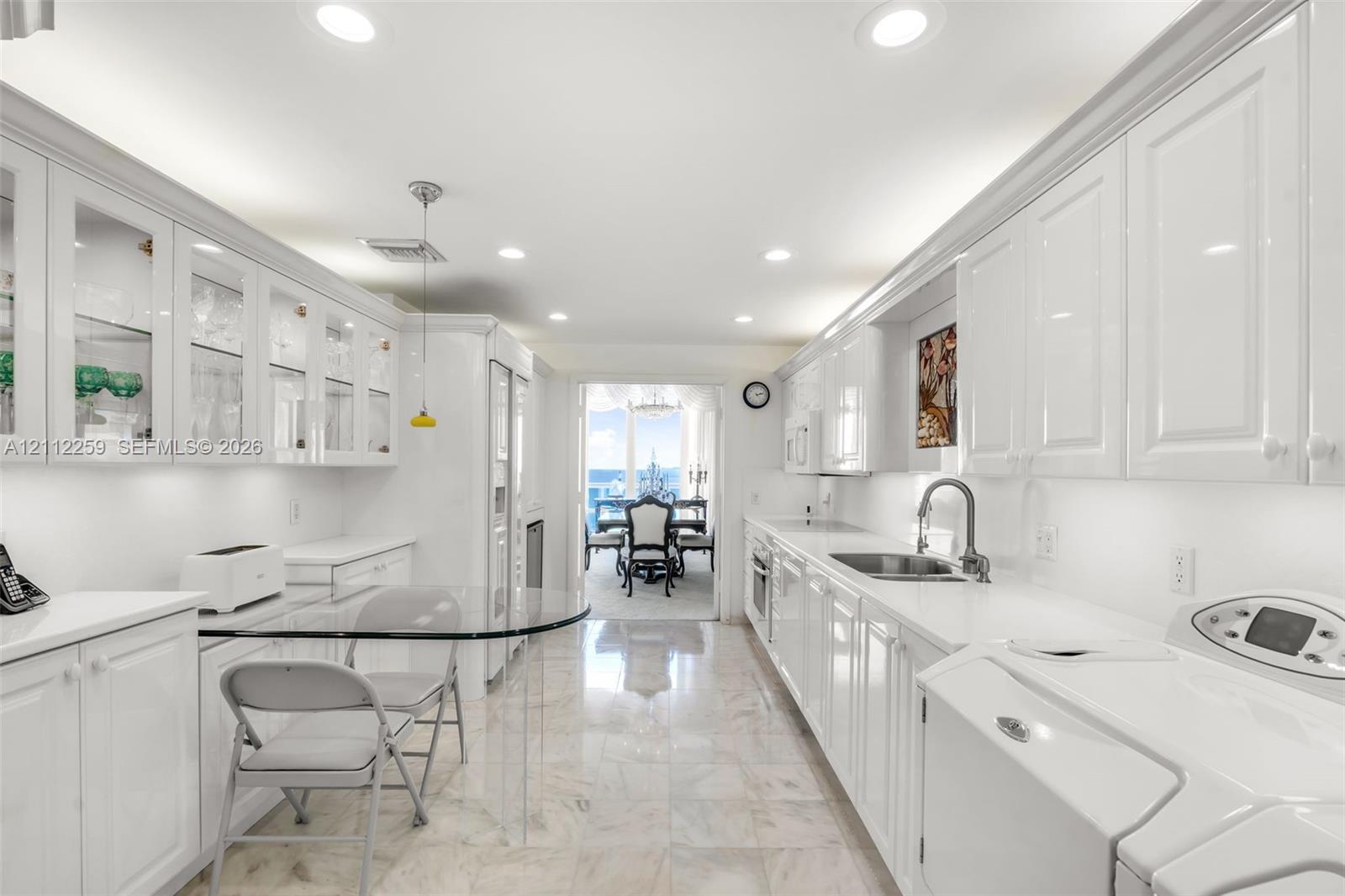 Galley-style kitchen featuring high-gloss white cabinetry, glass-front upper displays, stone-finish flooring, recessed lighting, and a single-basin undermount sink with a gooseneck faucet