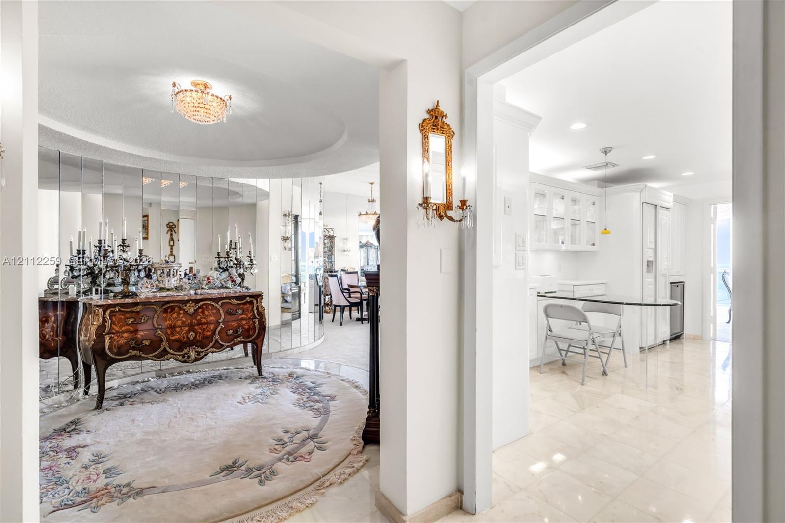 Foyer area featuring recessed tray ceiling, polished tile flooring, mirrored wall accents, and ornamental wall-mounted light fixtures
