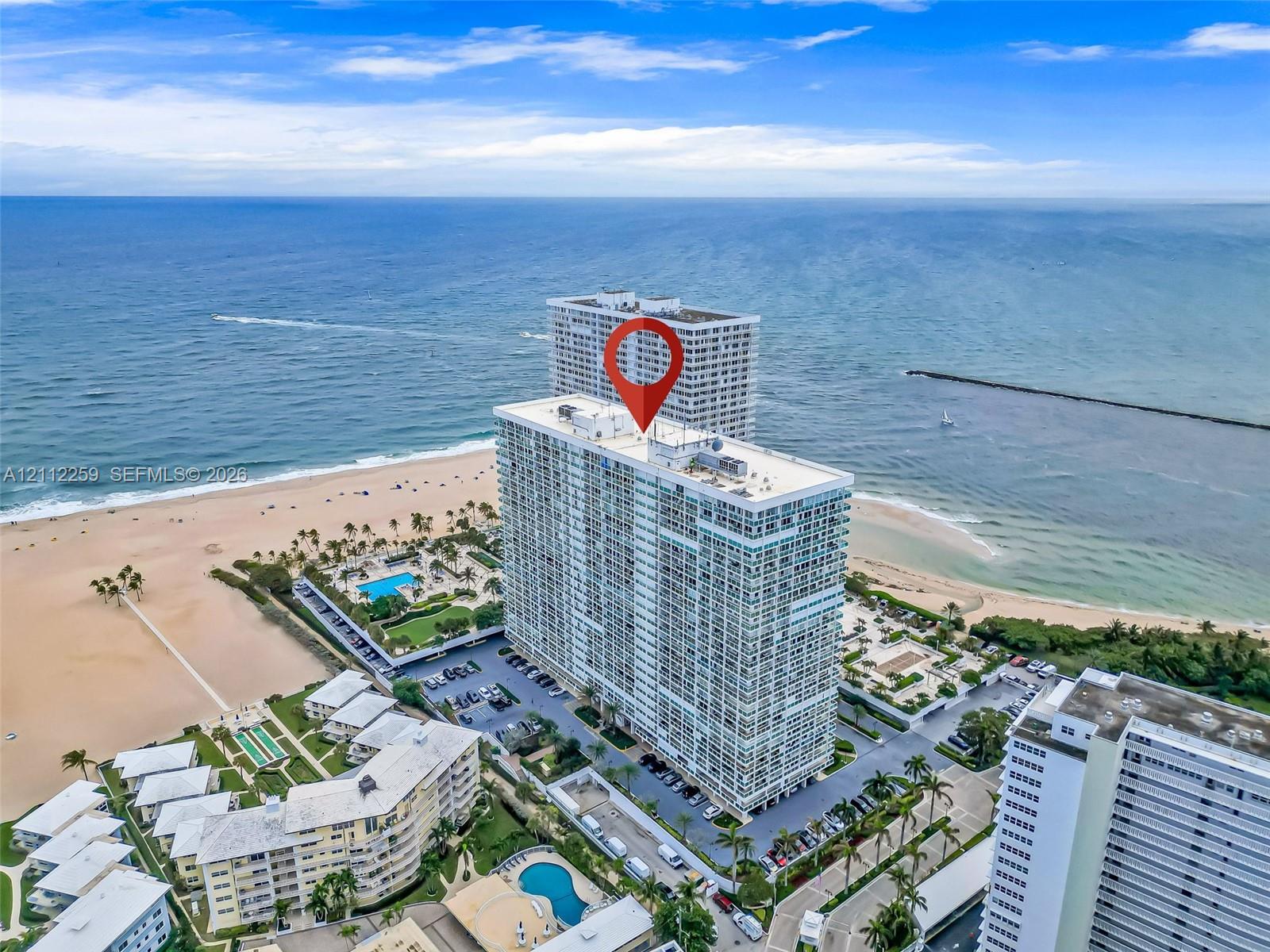 High-rise residential building situated directly on the coastline, featuring prominent ocean frontage, perimeter parking, and on-site swimming pools