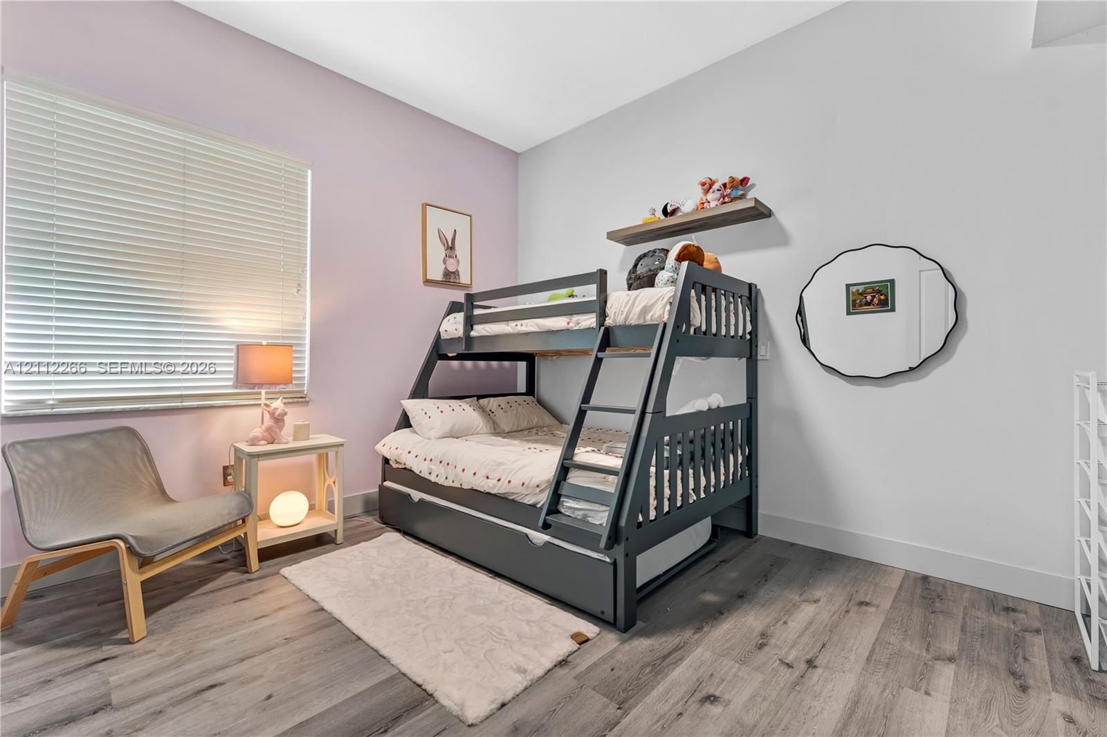 Neutral-toned room featuring wood-finish flooring, a wall-mounted floating shelf, and a window with horizontal blinds