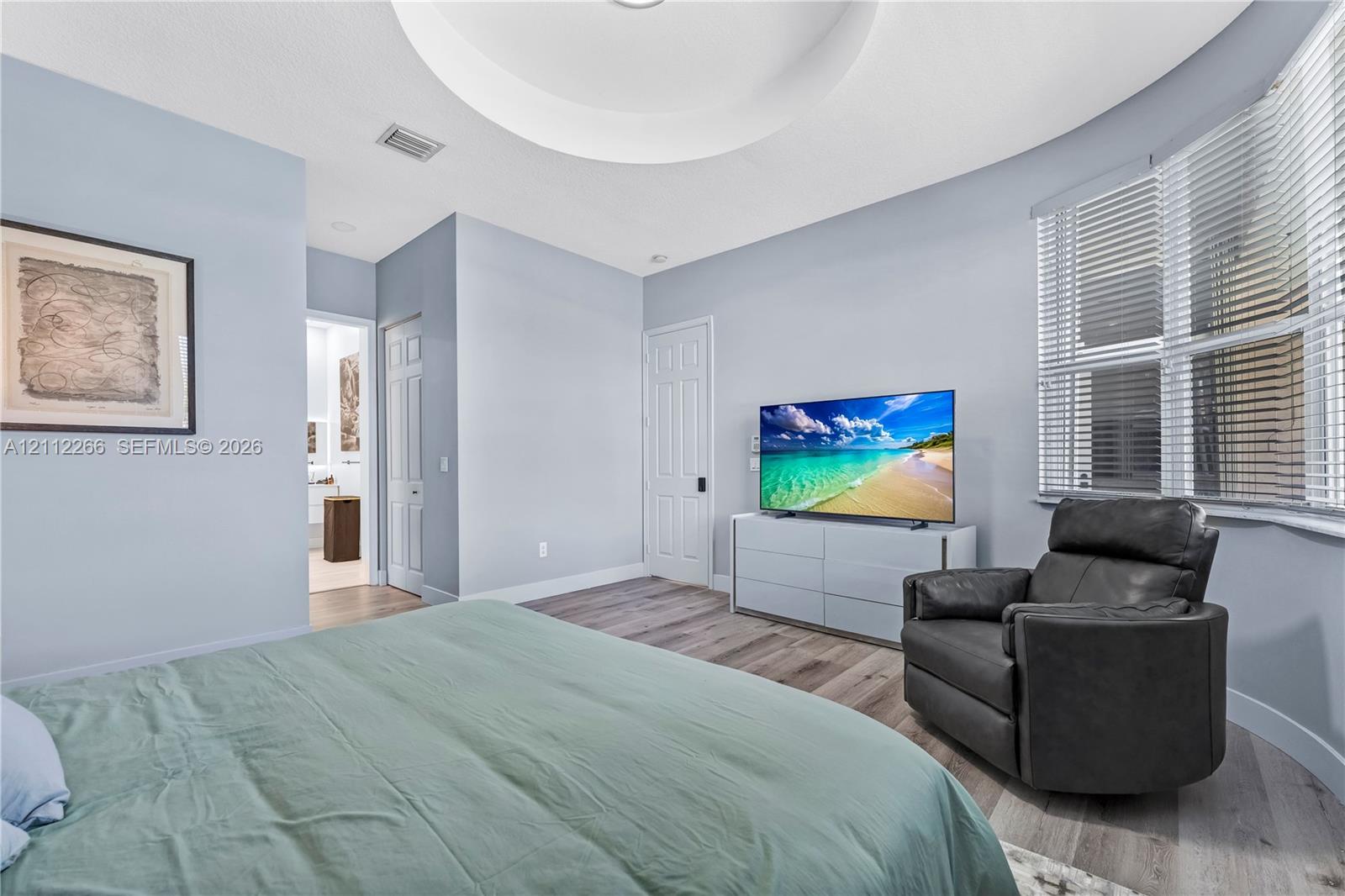 Tray ceiling with recessed lighting, wood-finish flooring, and expansive bay windows