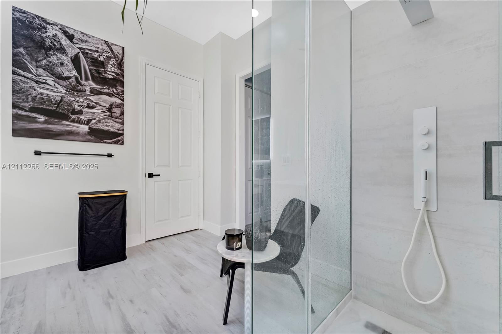 Walk-in shower featuring a glass enclosure, wall-mounted multi-function shower panel, and light-toned wood-finish flooring