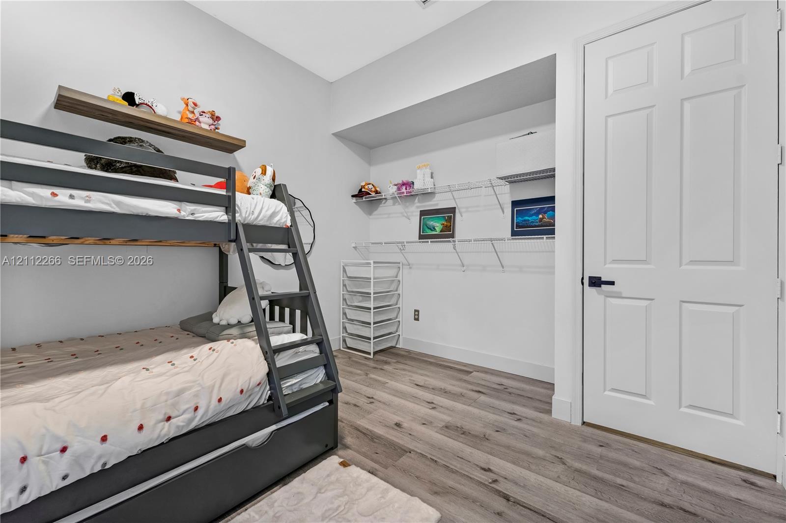 Wood-finish flooring, white four-panel interior door with matte black hardware, and built-in white wire shelving system