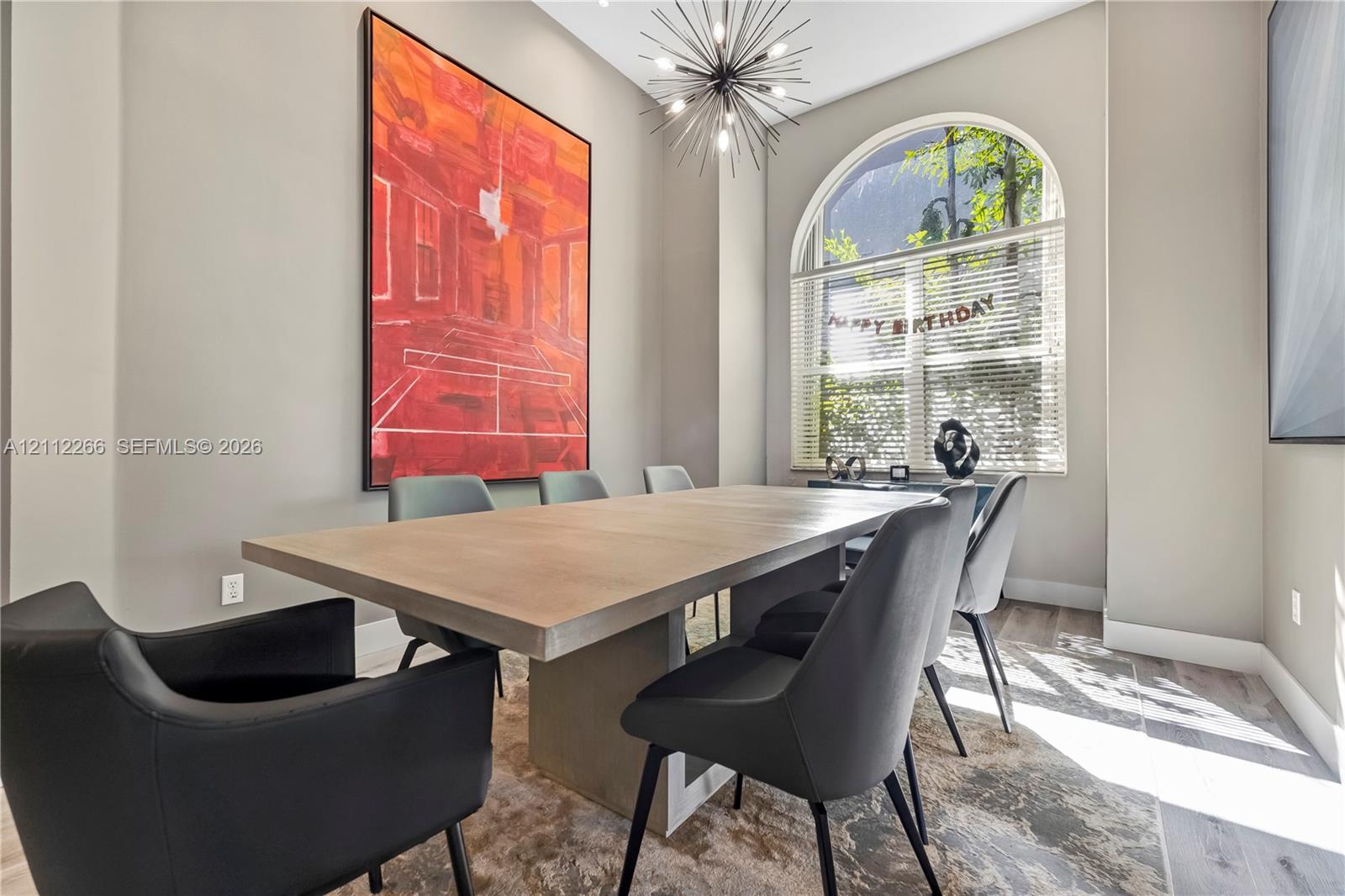 High-ceiling room featuring wood-finish flooring, a prominent arched window, and a multi-arm sputnik-style chandelier High-ceiling room featuring wood-finish flooring, a prominent arched window, and a multi-arm sputnik-style chandelier