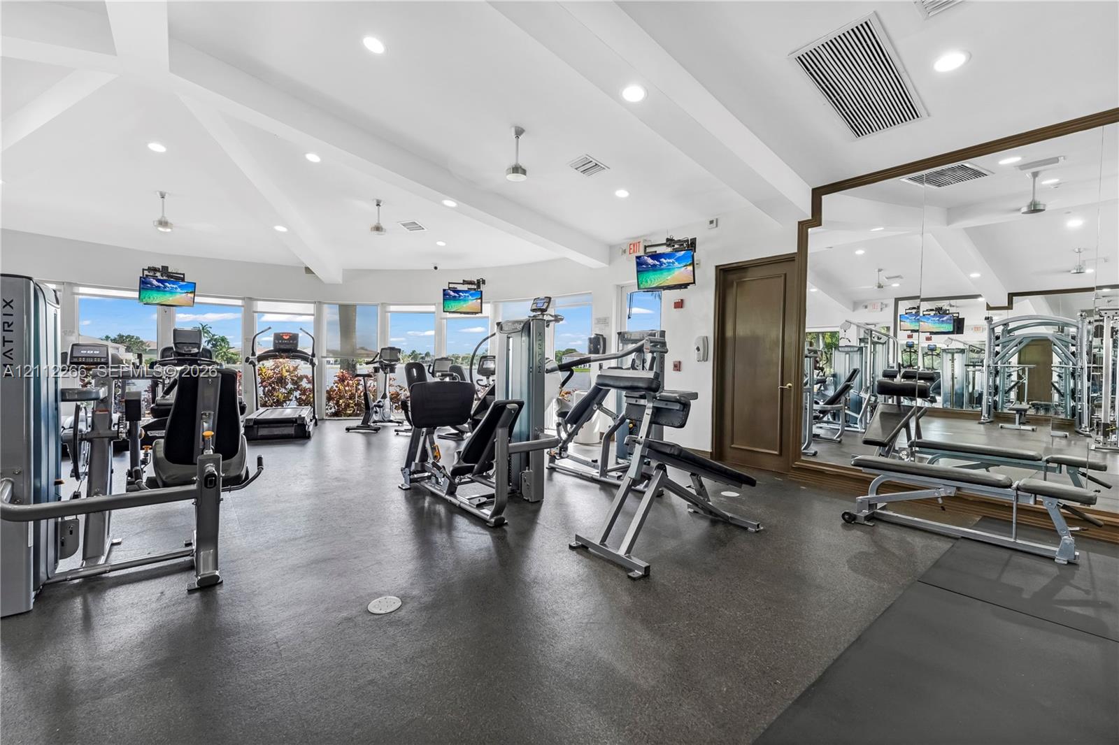 Fitness center featuring vaulted ceilings, floor-to-ceiling windows, full-wall mirrors, recessed lighting, and rubberized flooring