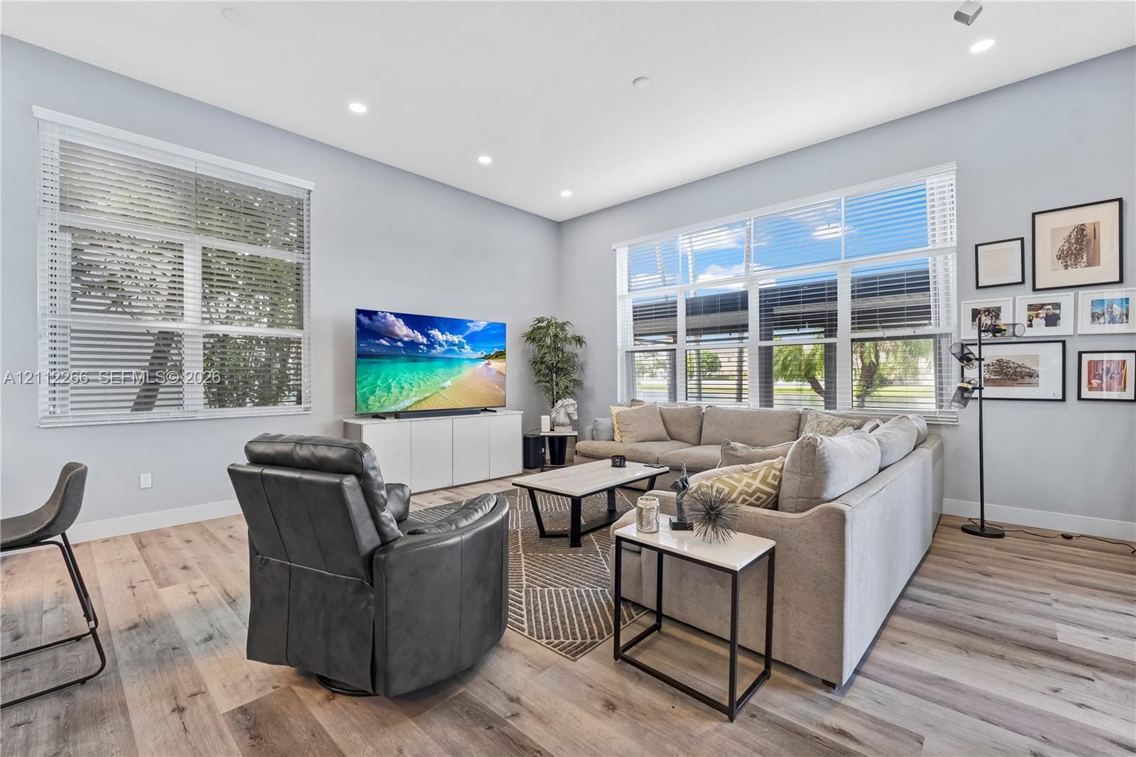 Living area featuring wide-plank wood-finish flooring, recessed lighting, and expansive windows with horizontal blinds