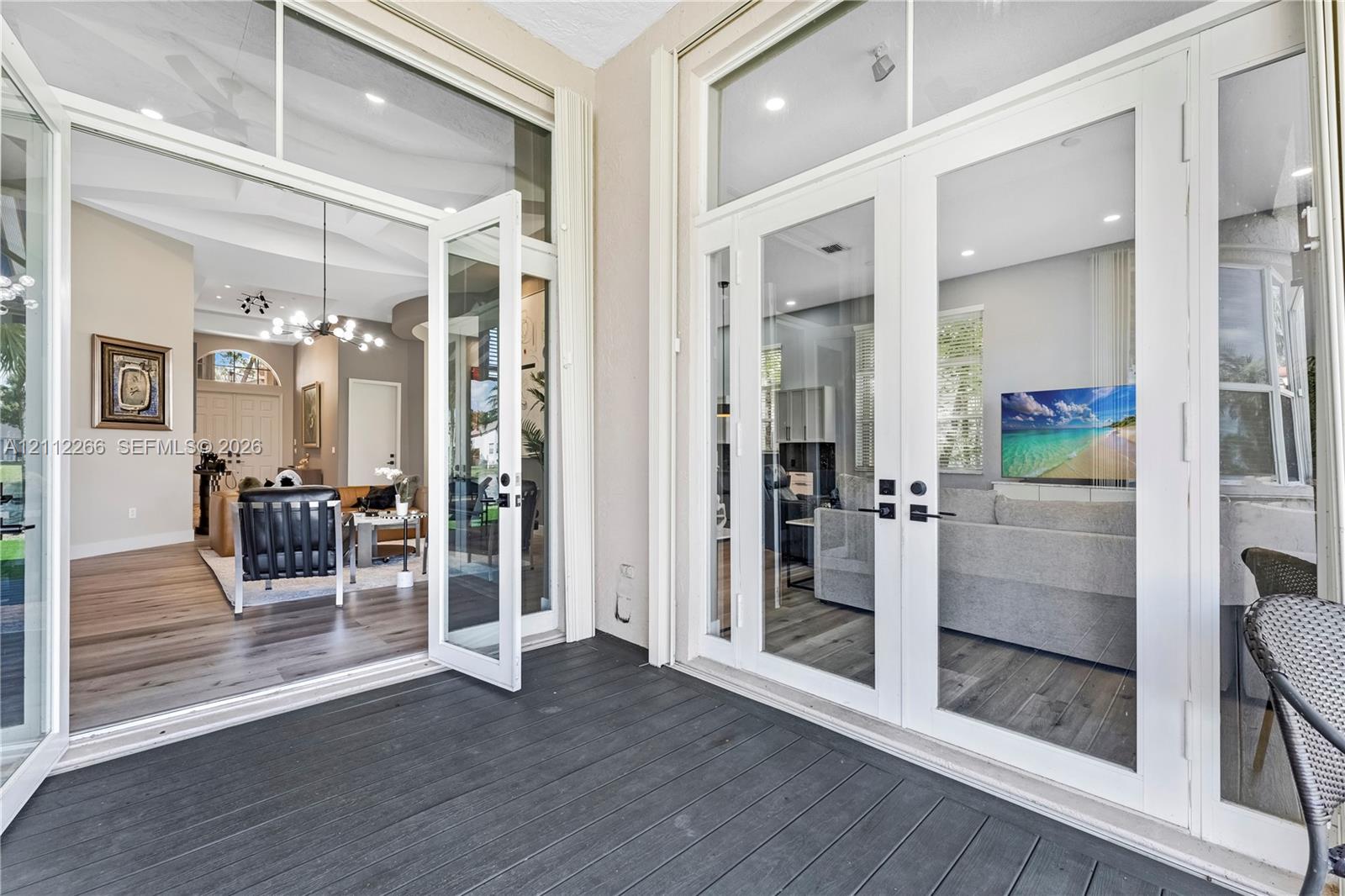 Covered patio featuring charcoal-tone composite decking and double glass-paneled entry doors with transom windows
