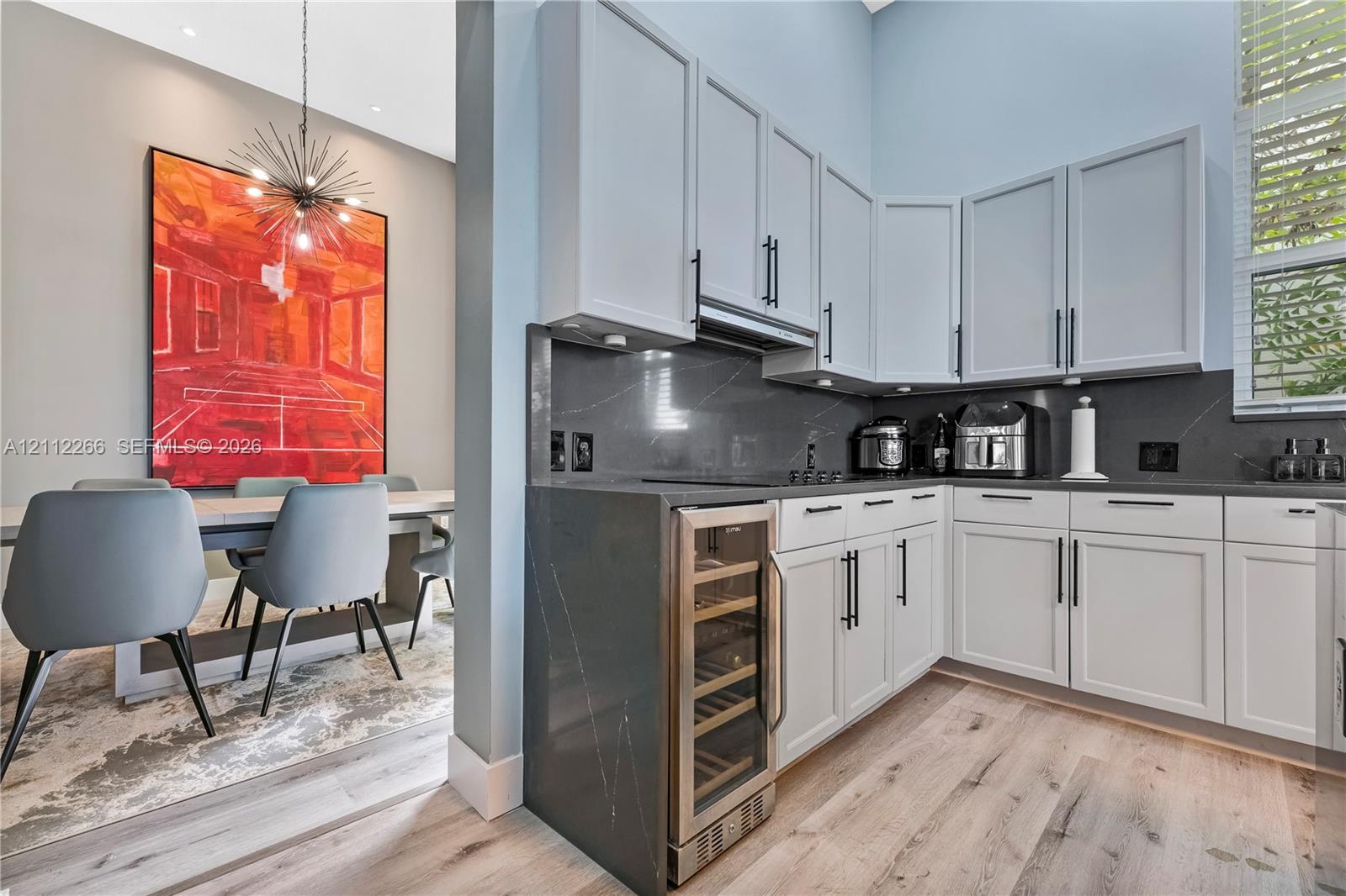 Kitchen featuring white shaker-style cabinetry, charcoal stone countertops, integrated wine refrigerator, and light wood-finish flooring Kitchen featuring white shaker-style cabinetry, charcoal stone countertops, integrated wine refrigerator, and light wood-finish flooring