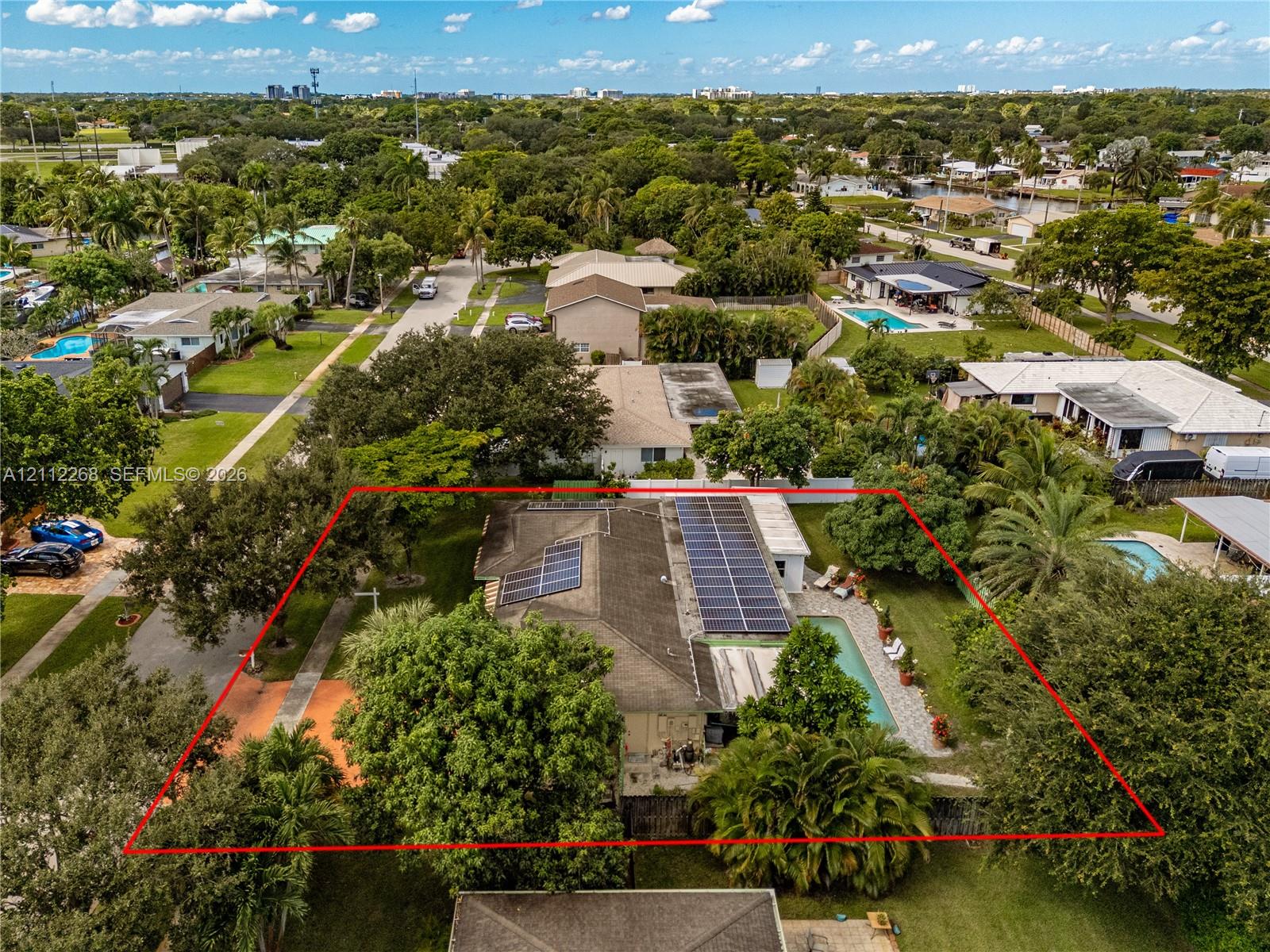 Aerial perspective of a property featuring roof-mounted solar panels, an in-ground swimming pool, and mature landscaping