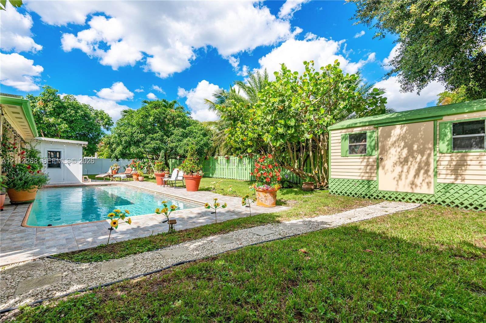 Backyard featuring a concrete-paver patio, swimming pool, detached storage structure, manicured lawn, and perimeter lattice fencing