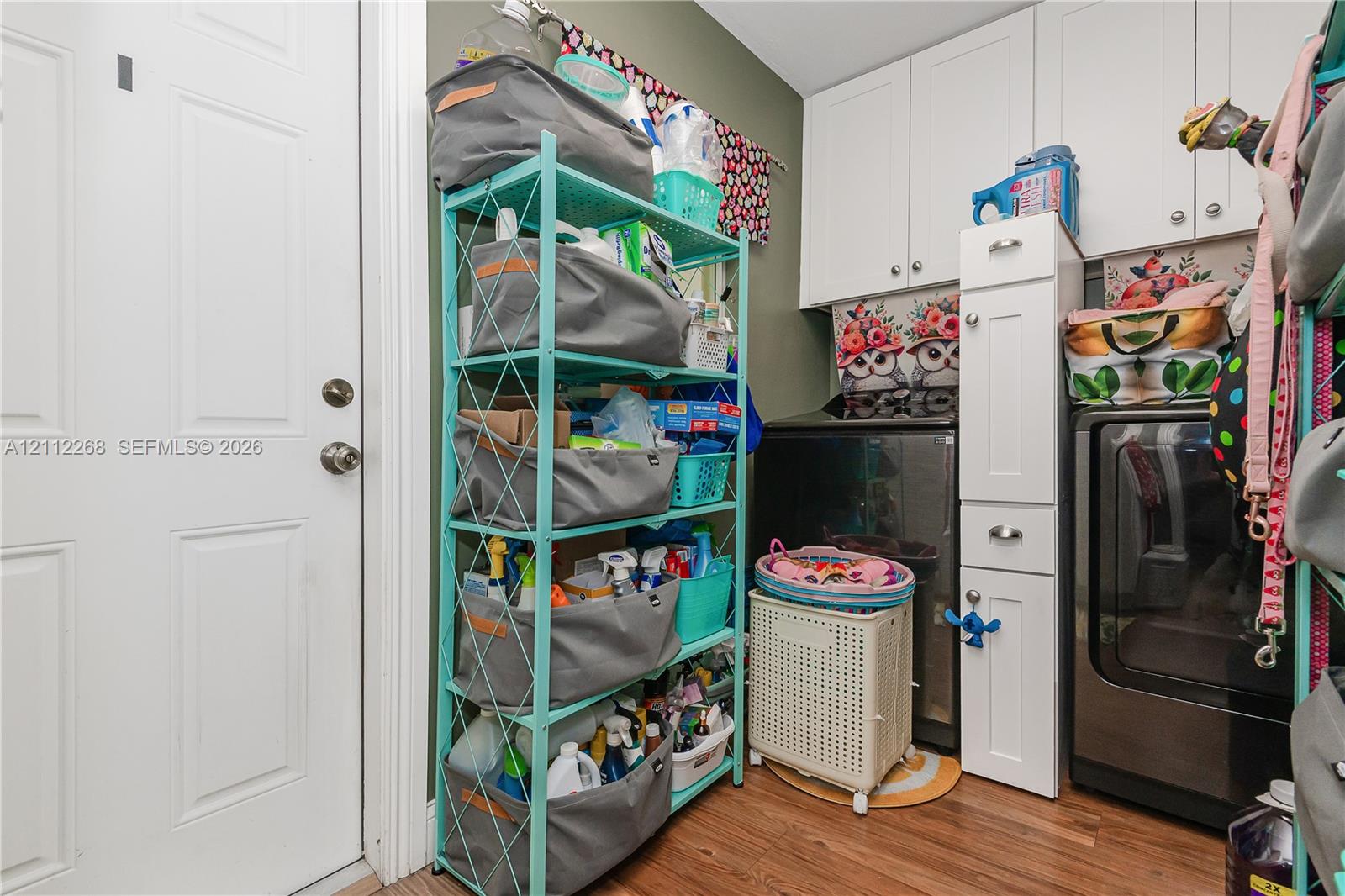 Laundry area featuring white shaker-style wall cabinets, a tall narrow storage tower with drawers, and wood-finish flooring