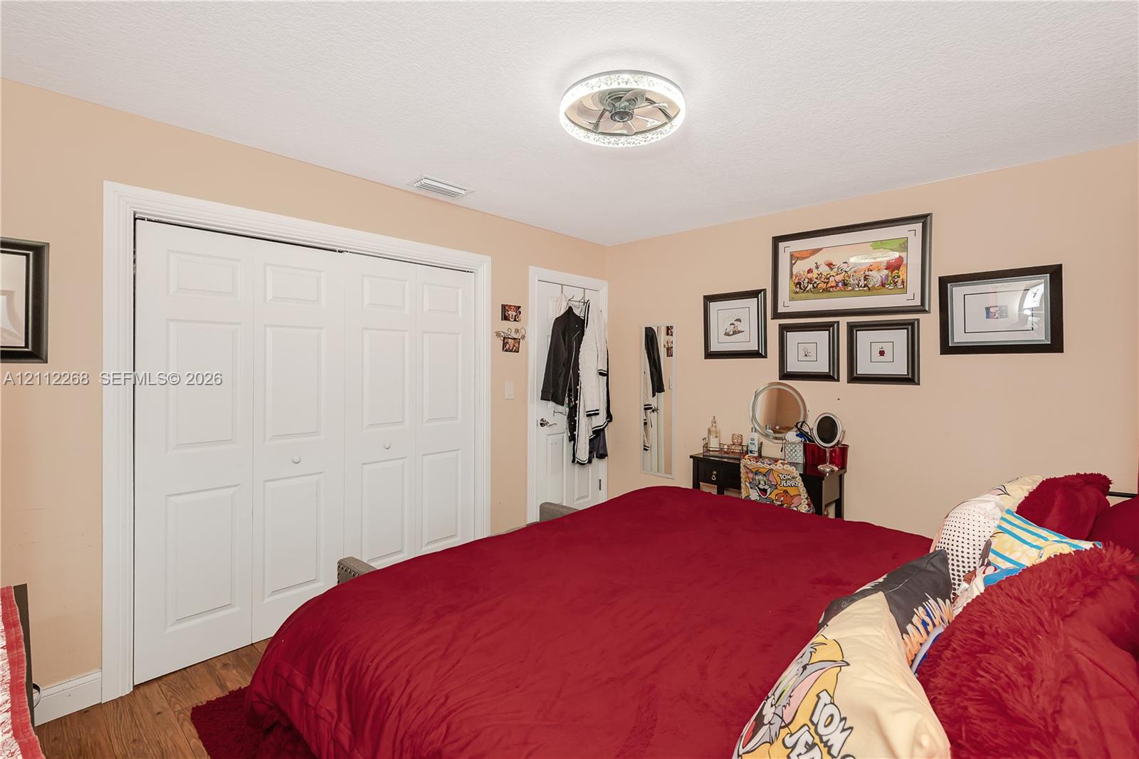 Bedroom featuring wood-finish flooring, a ceiling-mounted light fixture with a decorative rim, and bi-fold closet doors