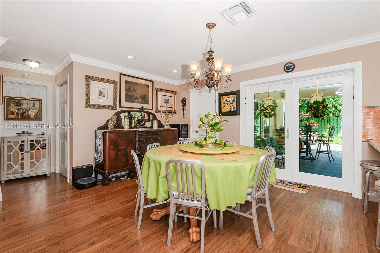 Dining area featuring wood-finish flooring, a decorative multi-arm chandelier, crown molding, and double-pane glass doors