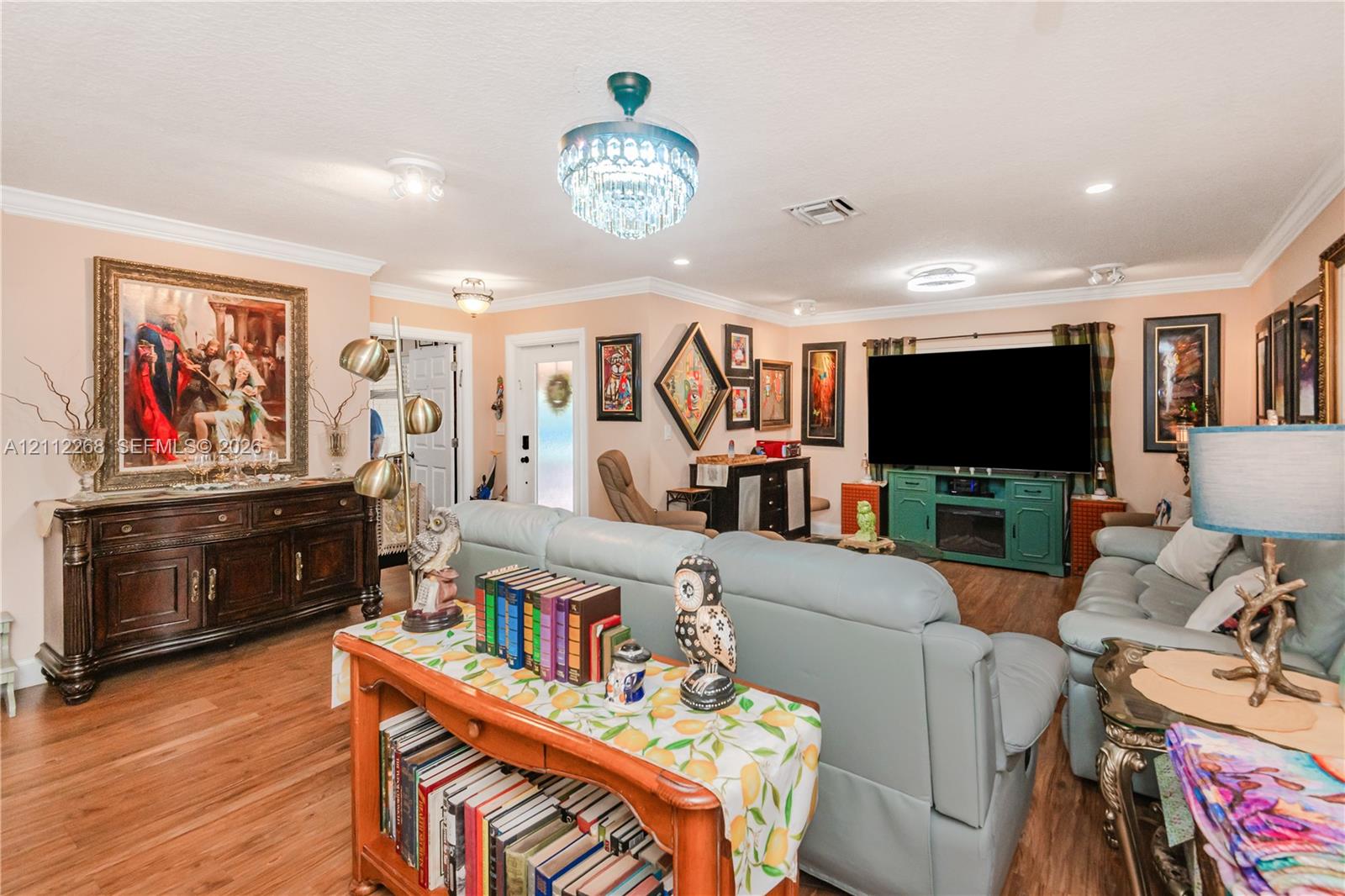 Living area featuring wood-finish flooring, a tiered crystal chandelier, crown molding, and a front entry door with a decorative glass insert