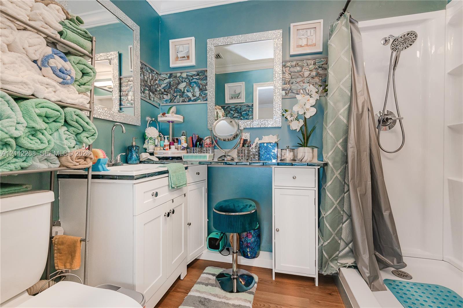 White vanity with integrated storage, decorative stone-tile backsplash, wall-mounted mirror with mosaic-style frame, and shower unit with handheld fixture