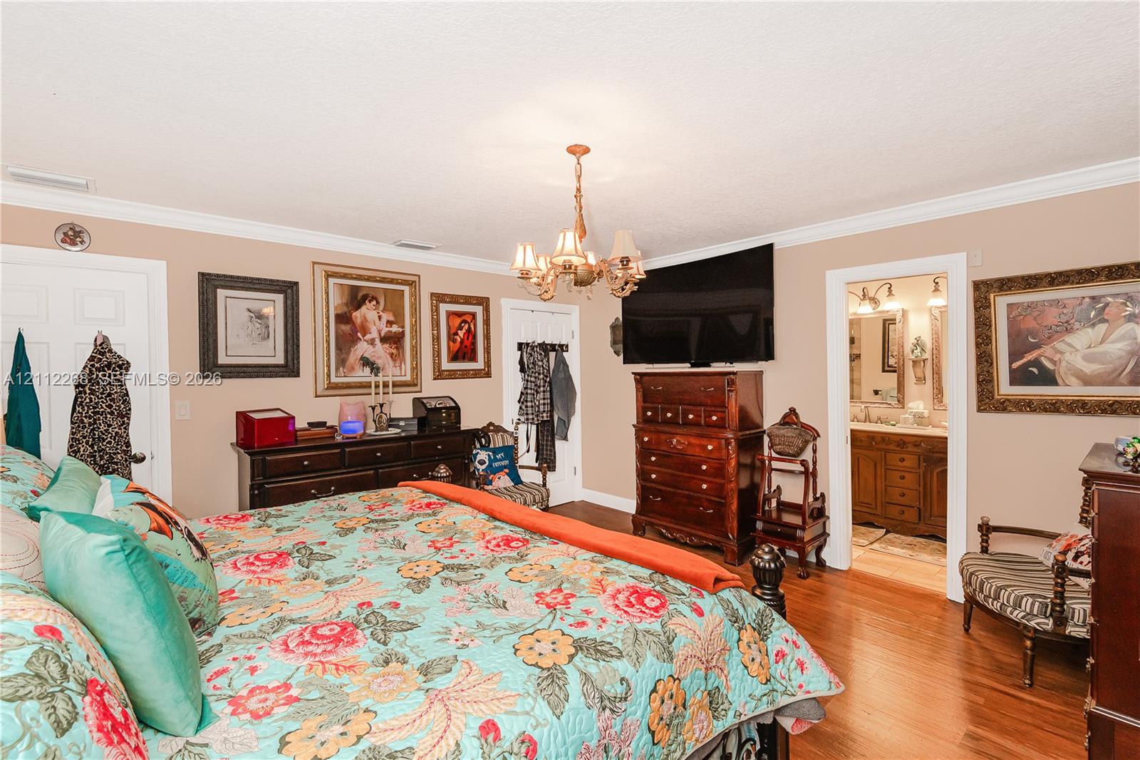 Room featuring wood-finish flooring, crown molding, and an ornate multi-arm chandelier