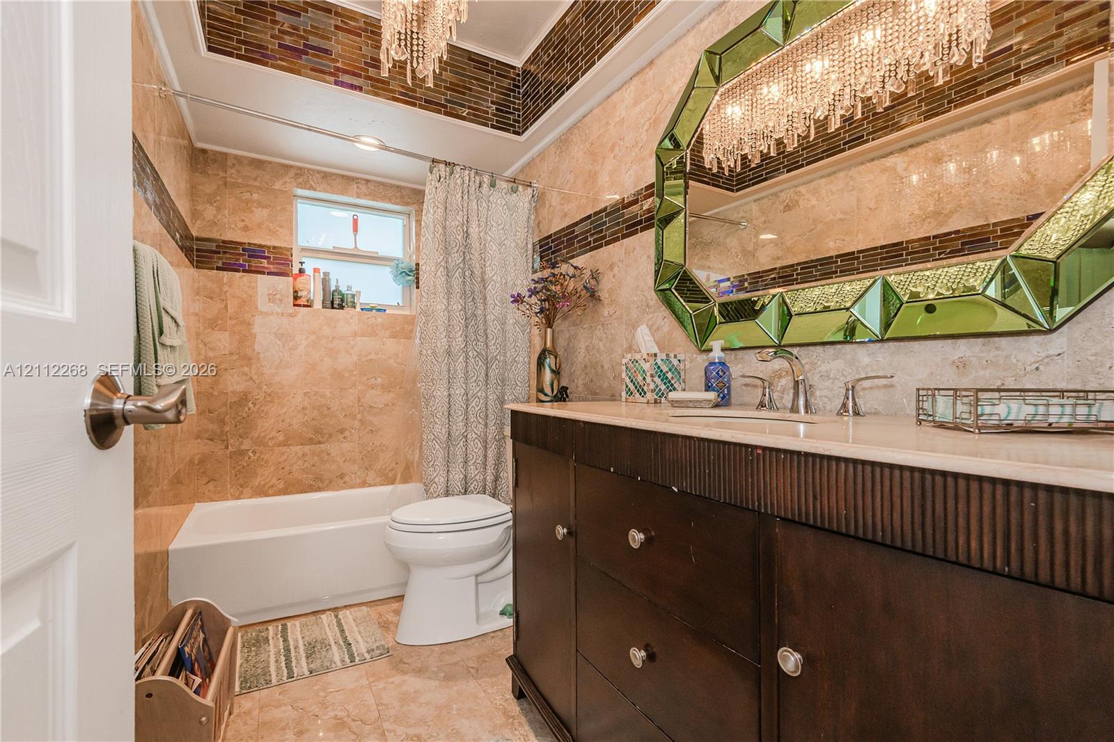 Bathroom featuring full-height wall tiling with decorative glass mosaic inlay, custom dark wood vanity with a solid surface countertop, and oversized framed mirror