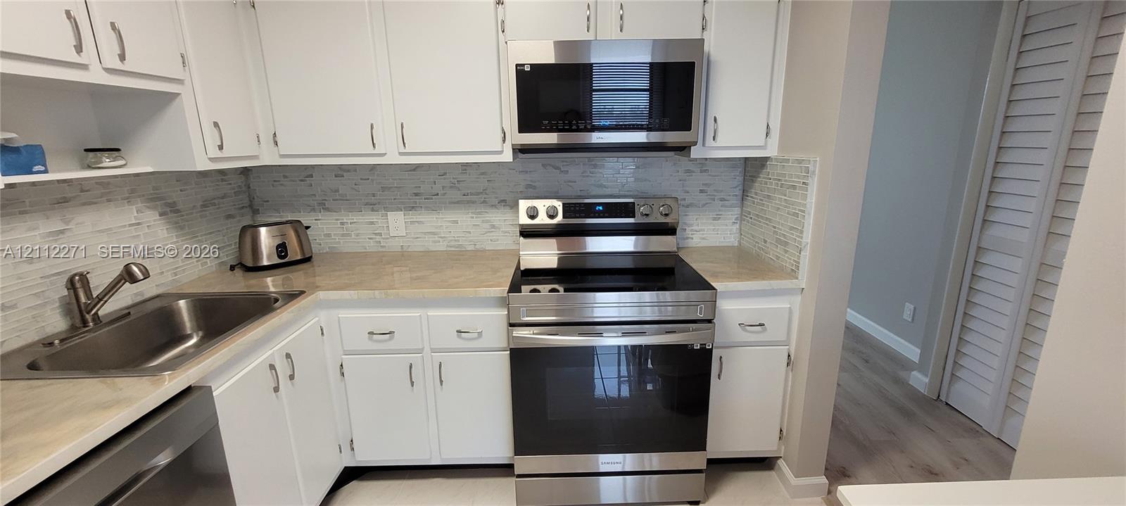 Kitchen featuring white shaker-style cabinetry, neutral countertops, stainless steel appliances, and a horizontal mosaic tile backsplash