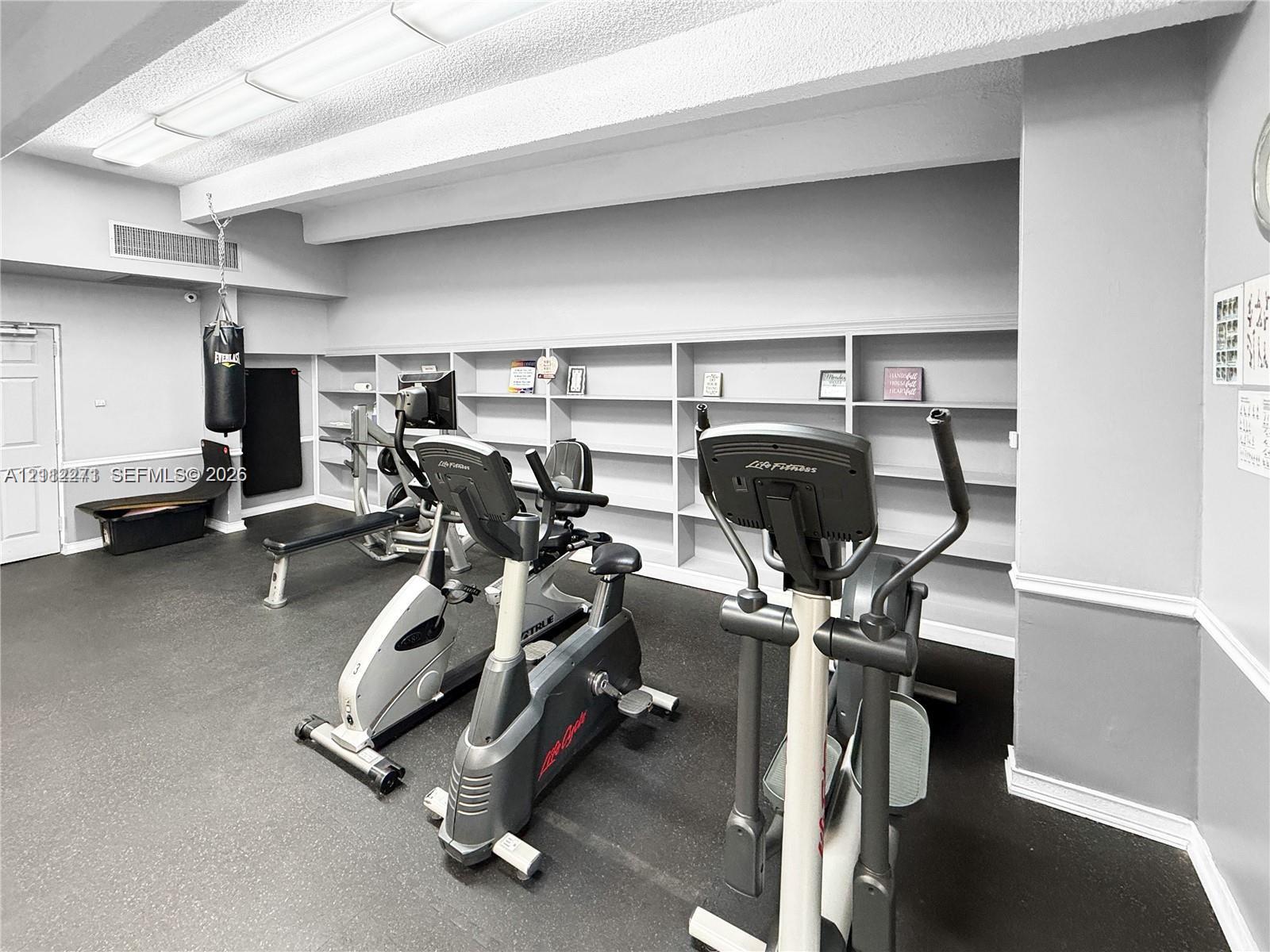 Fitness area featuring wall-to-wall built-in shelving, resilient rubber flooring, and recessed ceiling lighting