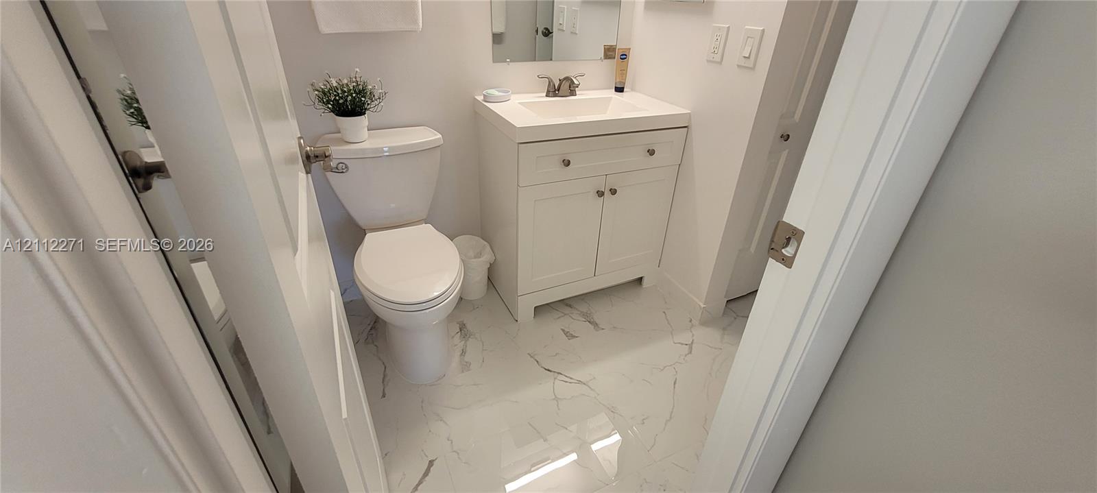 Bathroom featuring a white vanity cabinet with a integrated sink, polished stone-finish flooring with vein detailing, a dual-flush toilet, and a wall-mounted mirror